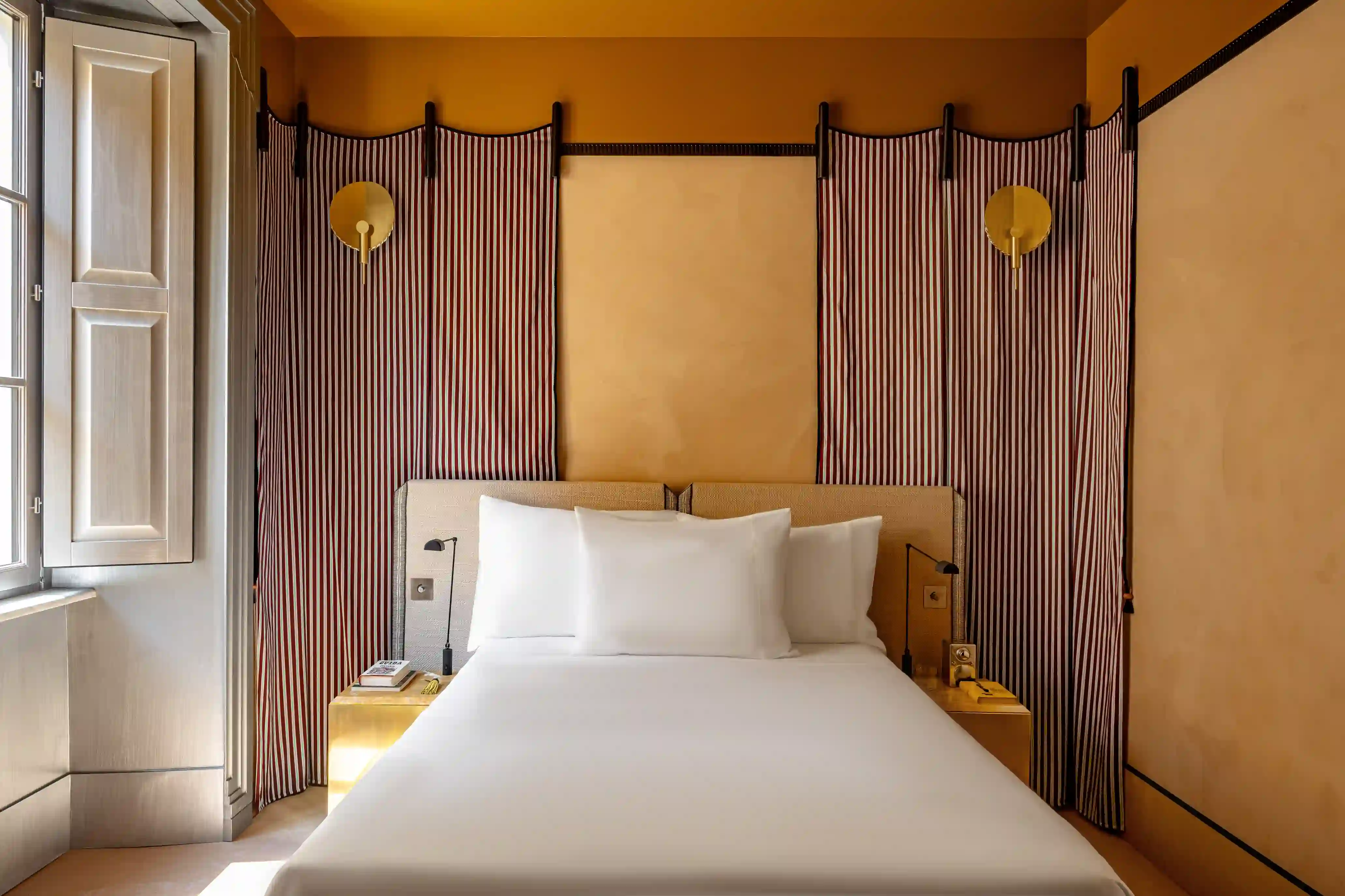 Hotel bedroom with white bedding, mustard yellow nightstand and sculptural globe wall sconce at Experimental Roma, Experimental Group.