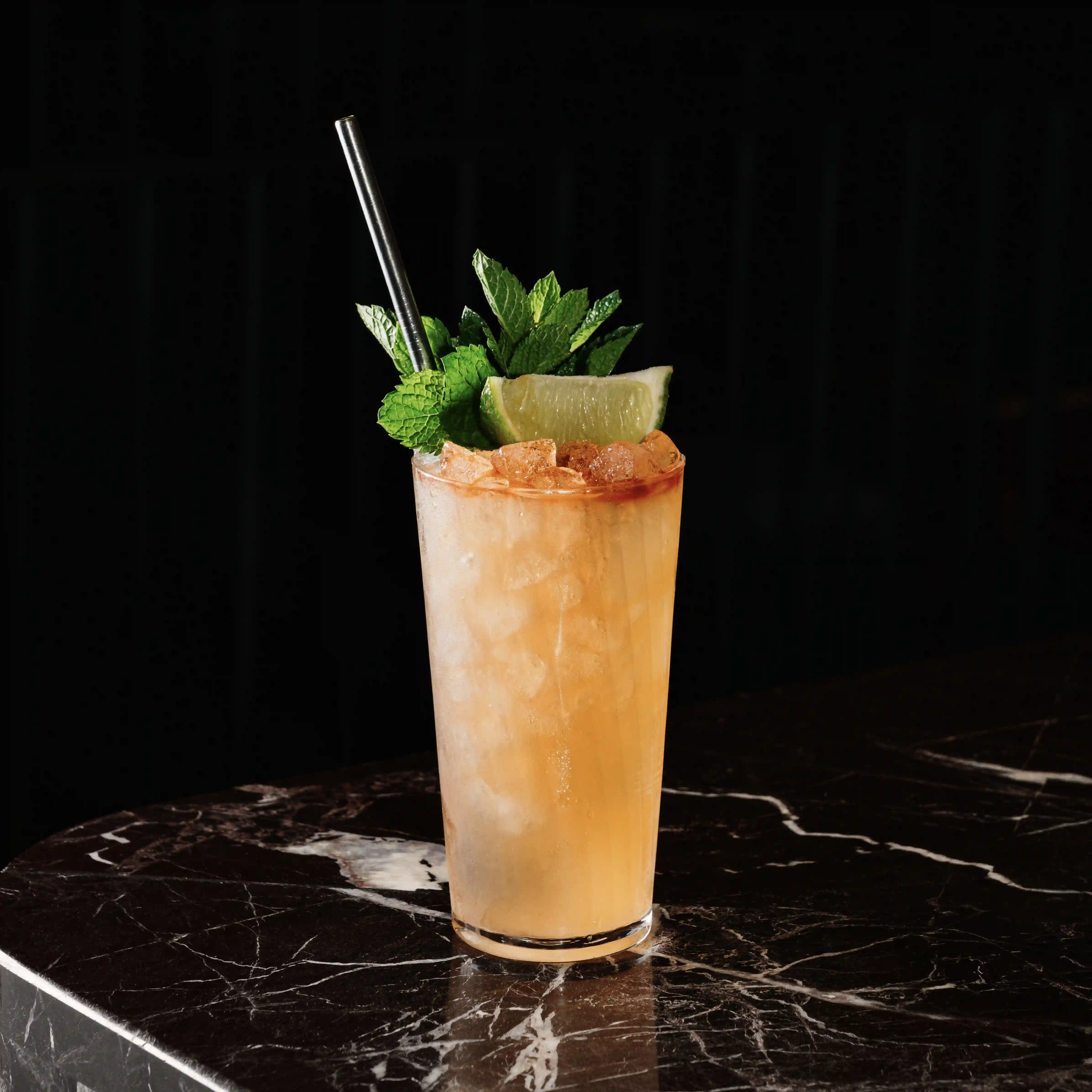 A refreshing cocktail in a highball glass, garnished with fresh mint and a lime wedge, set on a dark stone surface.