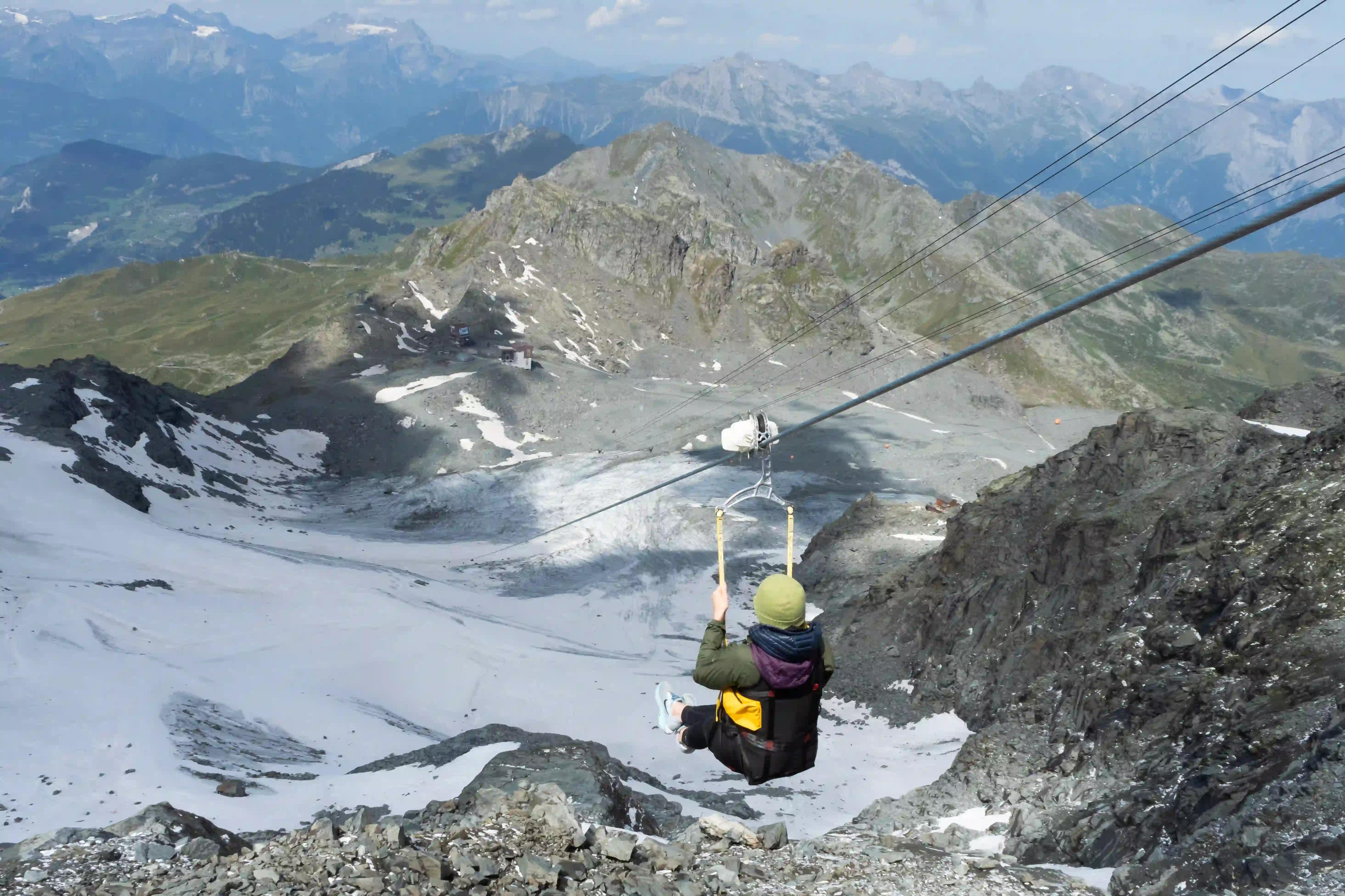A person on a zipline adventure above a scenic, rugged mountain range with snowy peaks.