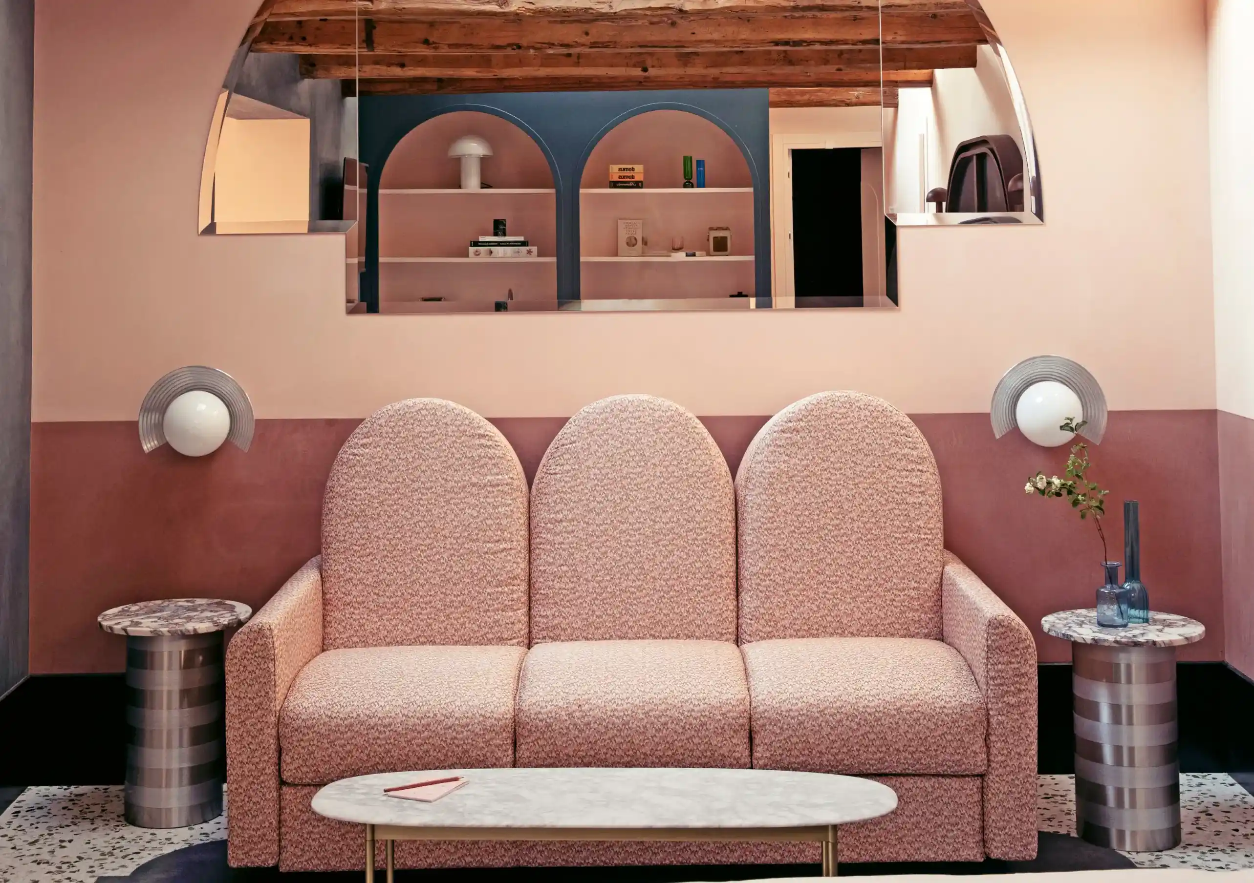 Il Palazzo Experimental suite lounge with triple-arched pink boucle sofa, globe wall sconces and arched shelving mirror in Venice.