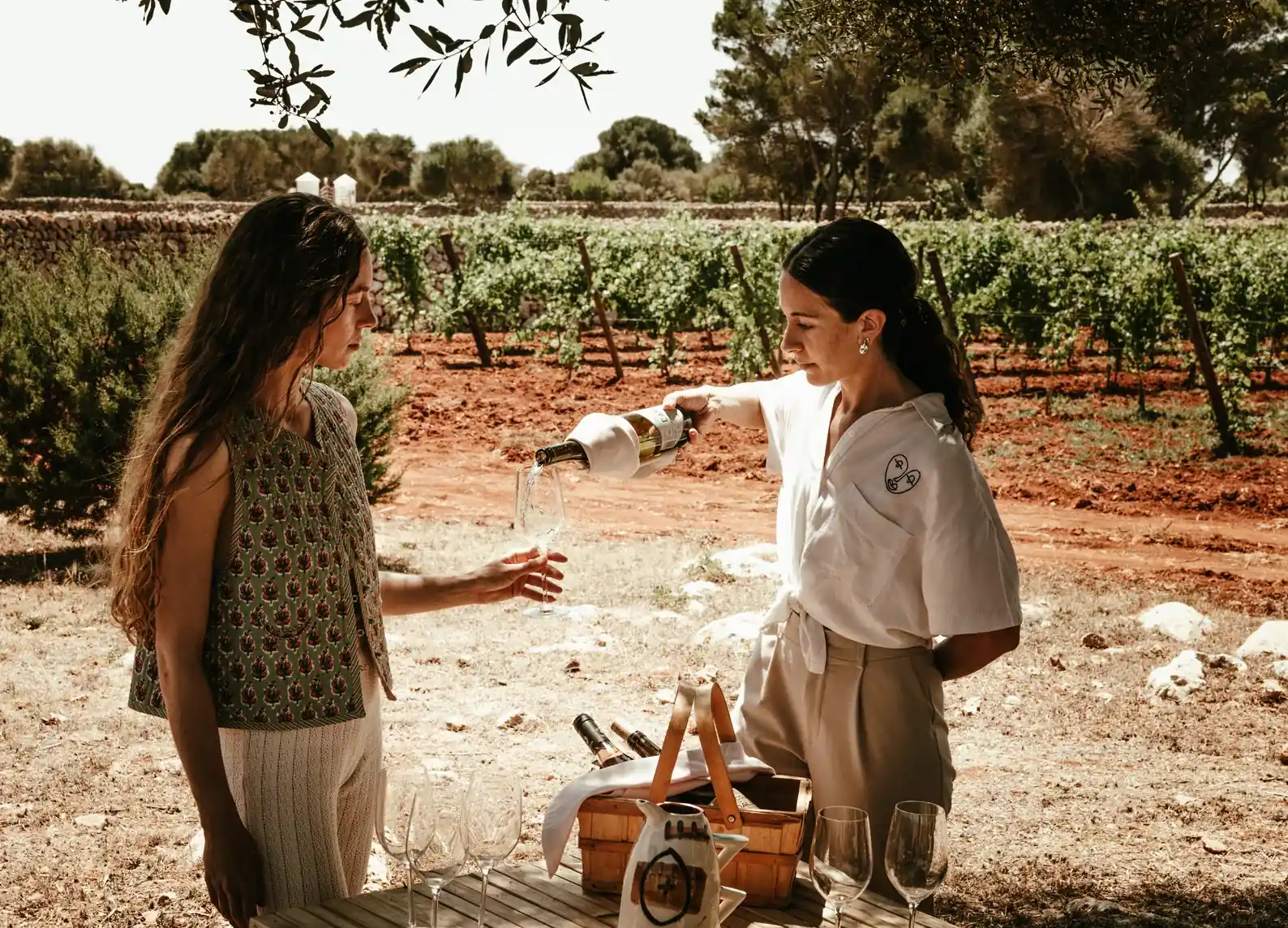 Two women enjoying a picnic with wine in a sunny vineyard.