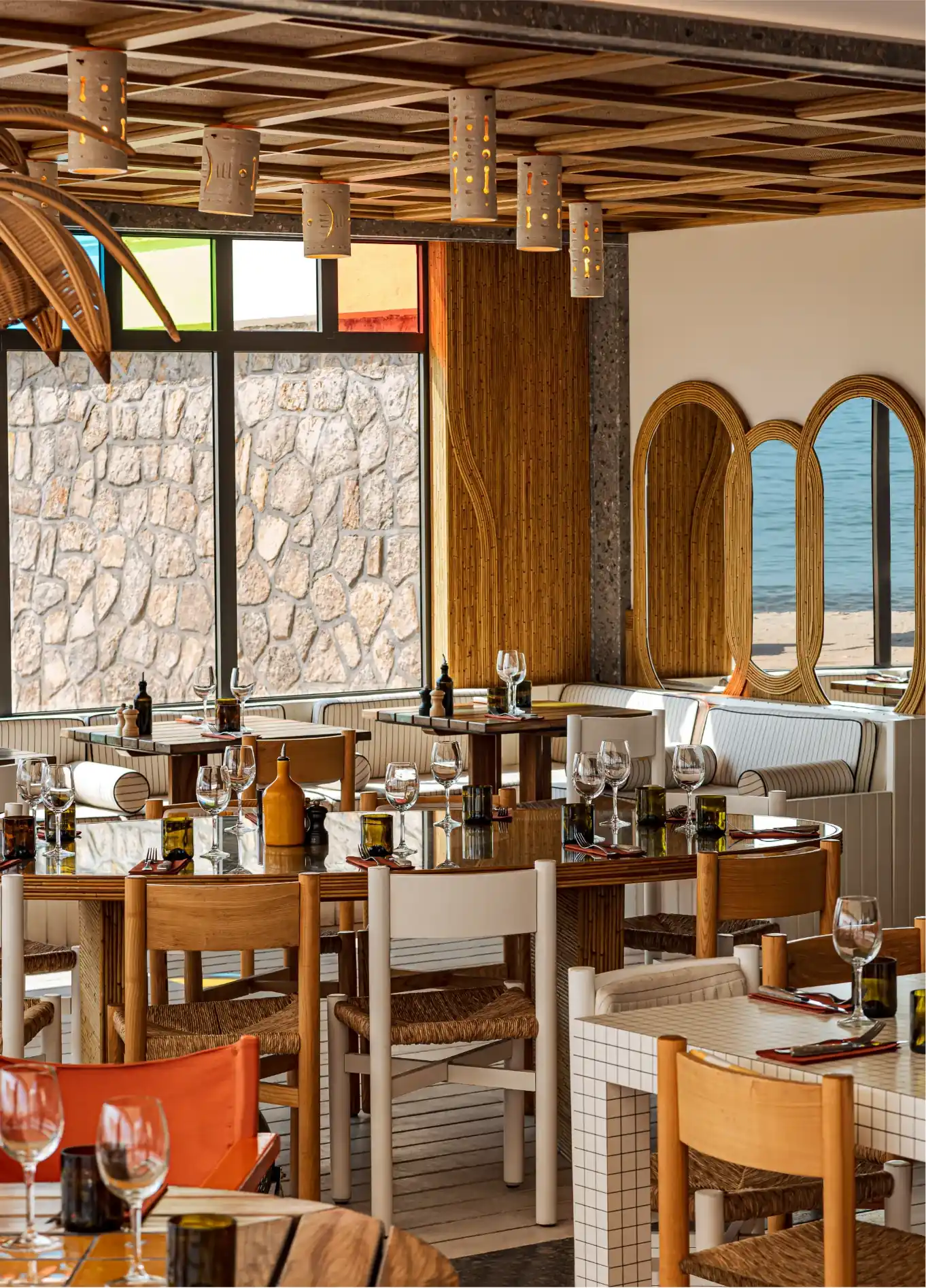 Cozy restaurant interior with wooden chairs, set tables, large windows, and decorative mirrors.
