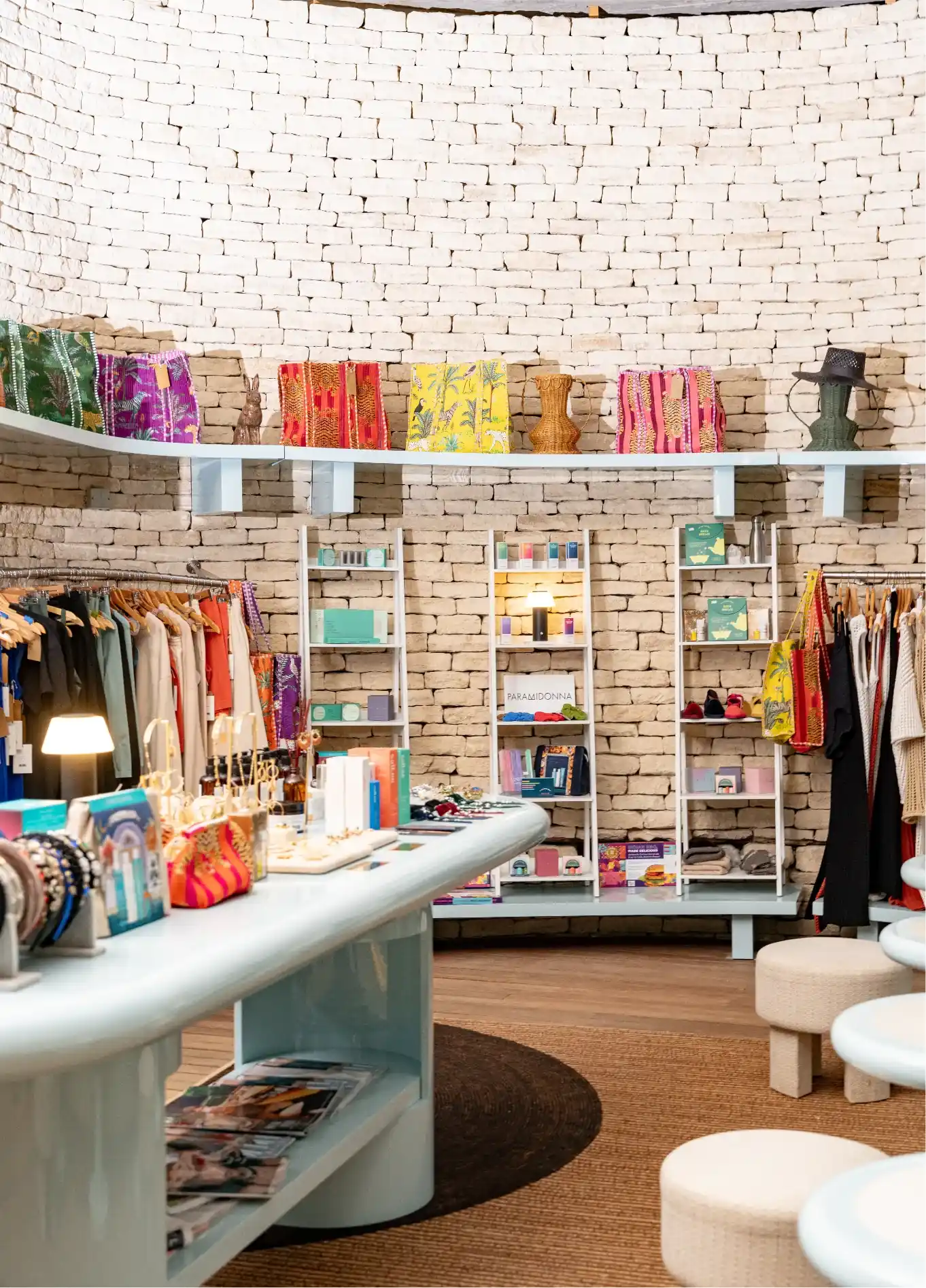 Boutique interior with stone walls displaying colorful bags, clothing racks, and jewelry on counters.