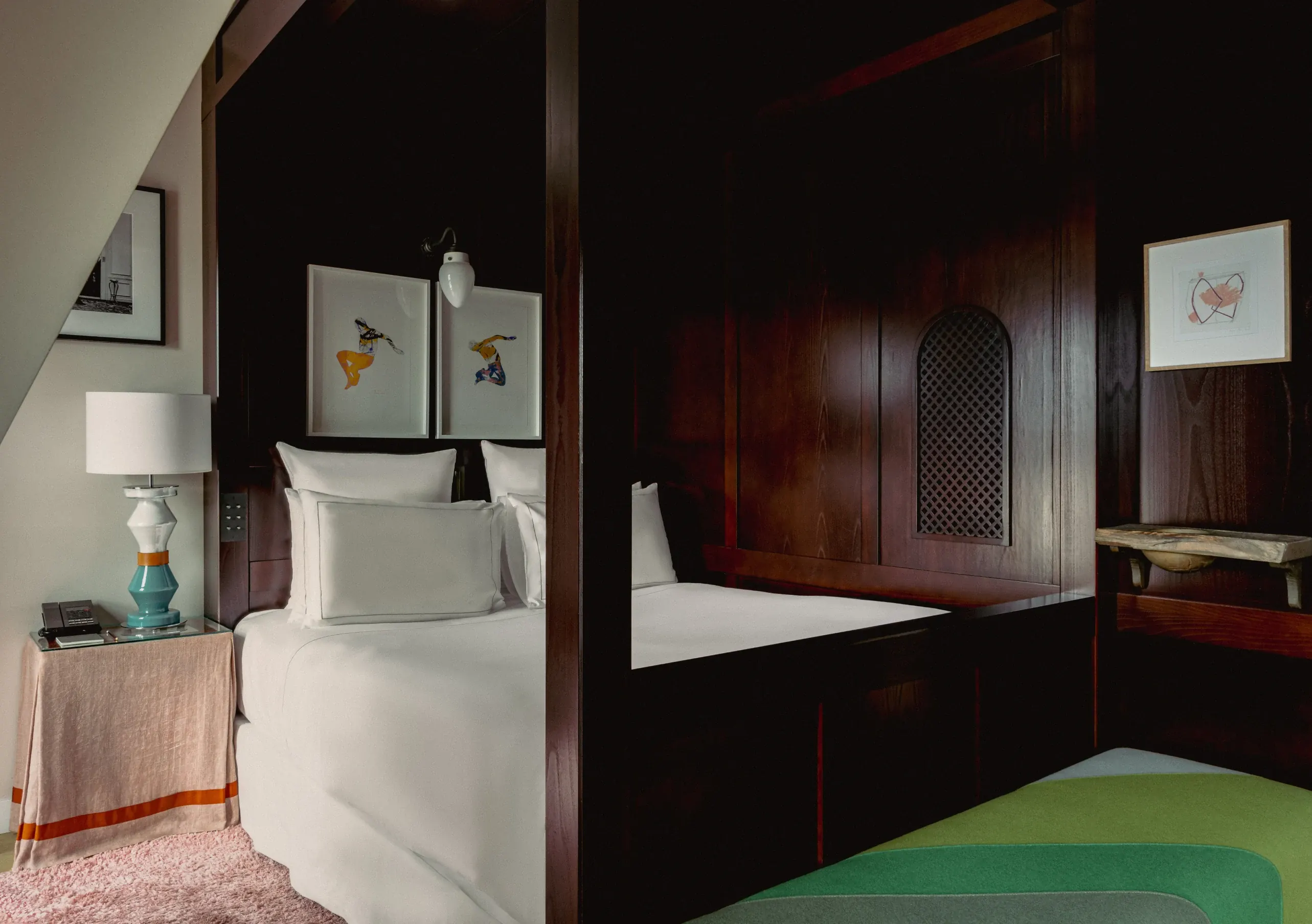 Hotel room with white bed, dark wooden four-poster frame, bedside lamp, and abstract wall art.