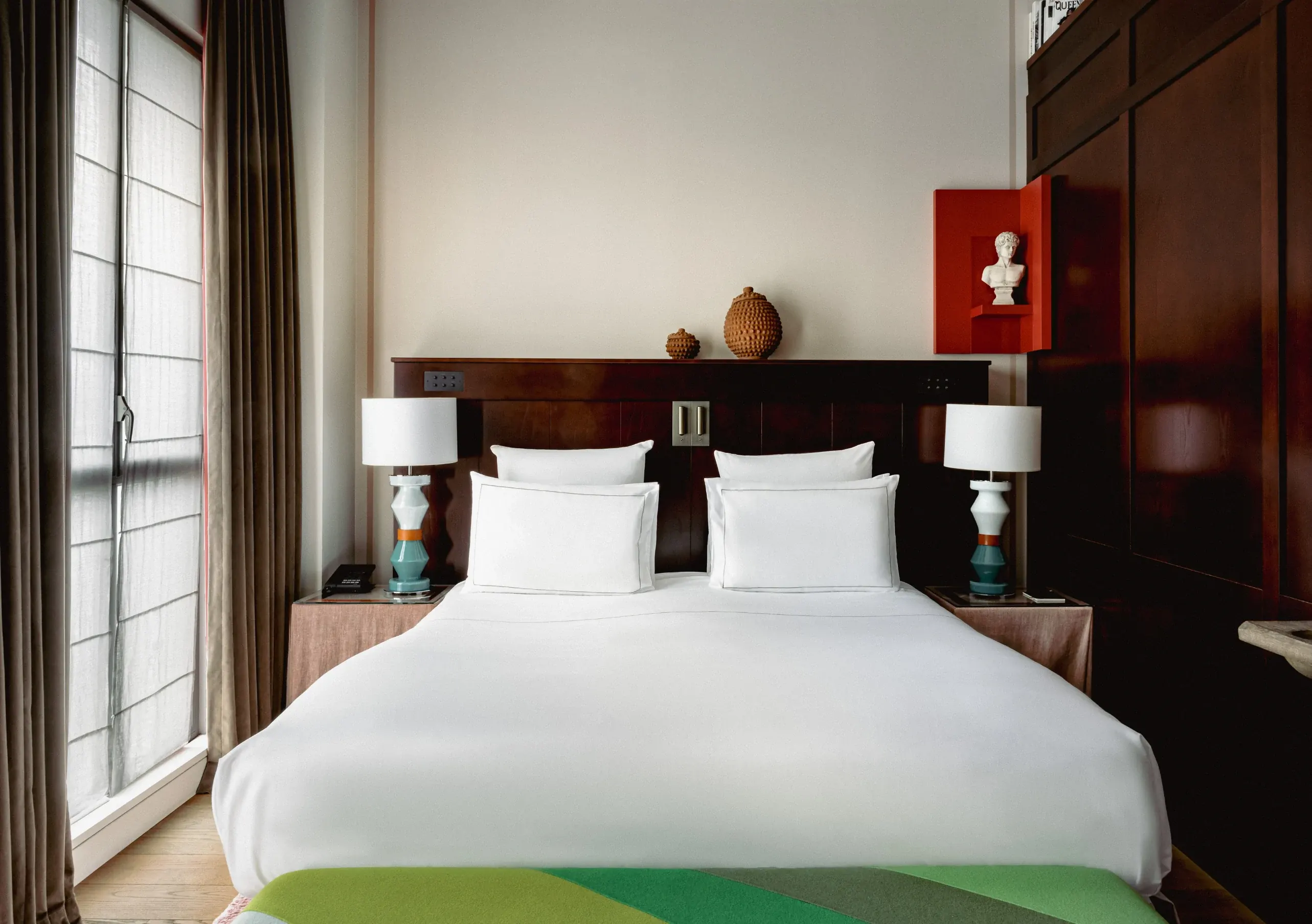 Modern hotel room with large bed, white linens, patterned lamps, and decorative vases and bust.