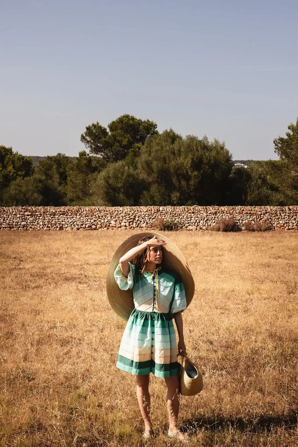 Woman in striped dress and large straw hat in a dry field at Menorca Experimental.