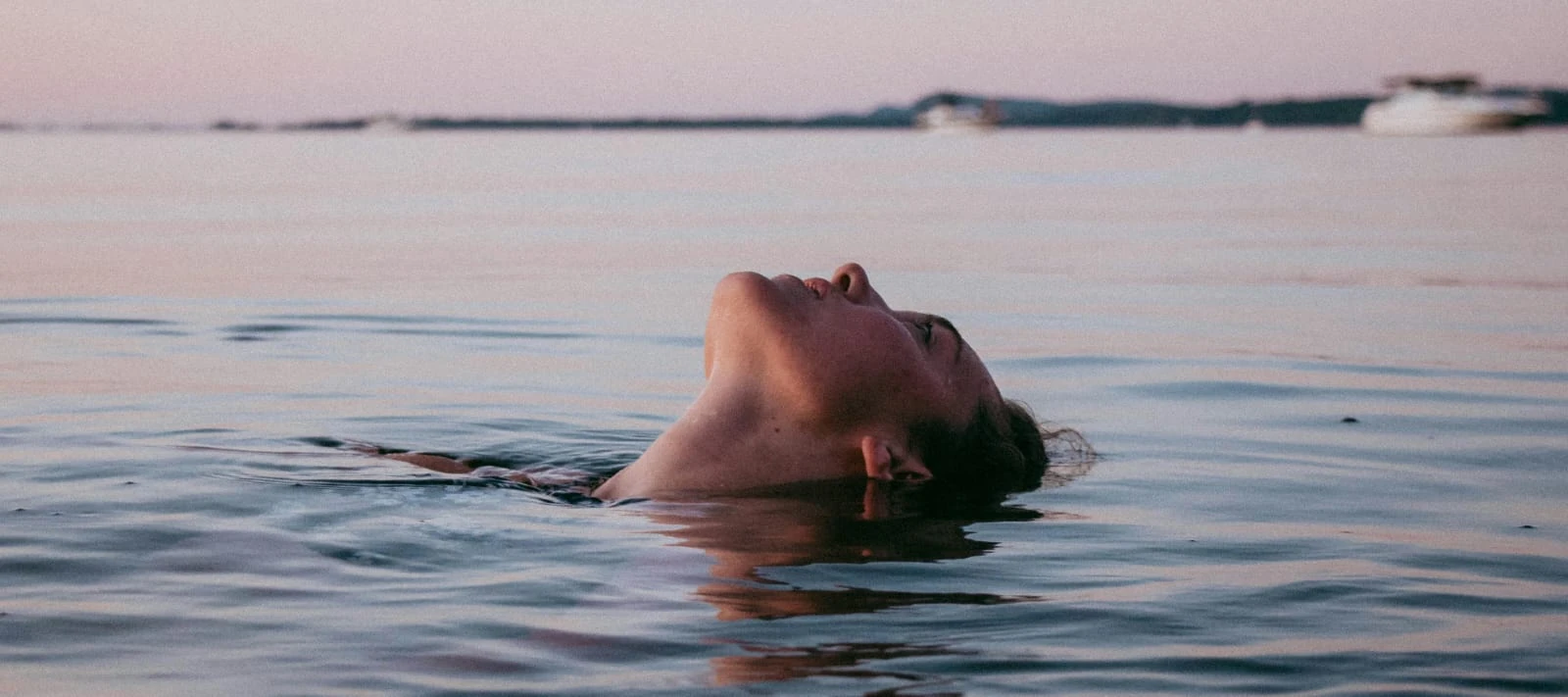 Person floating on their back in calm water with head tilted back at sunset.