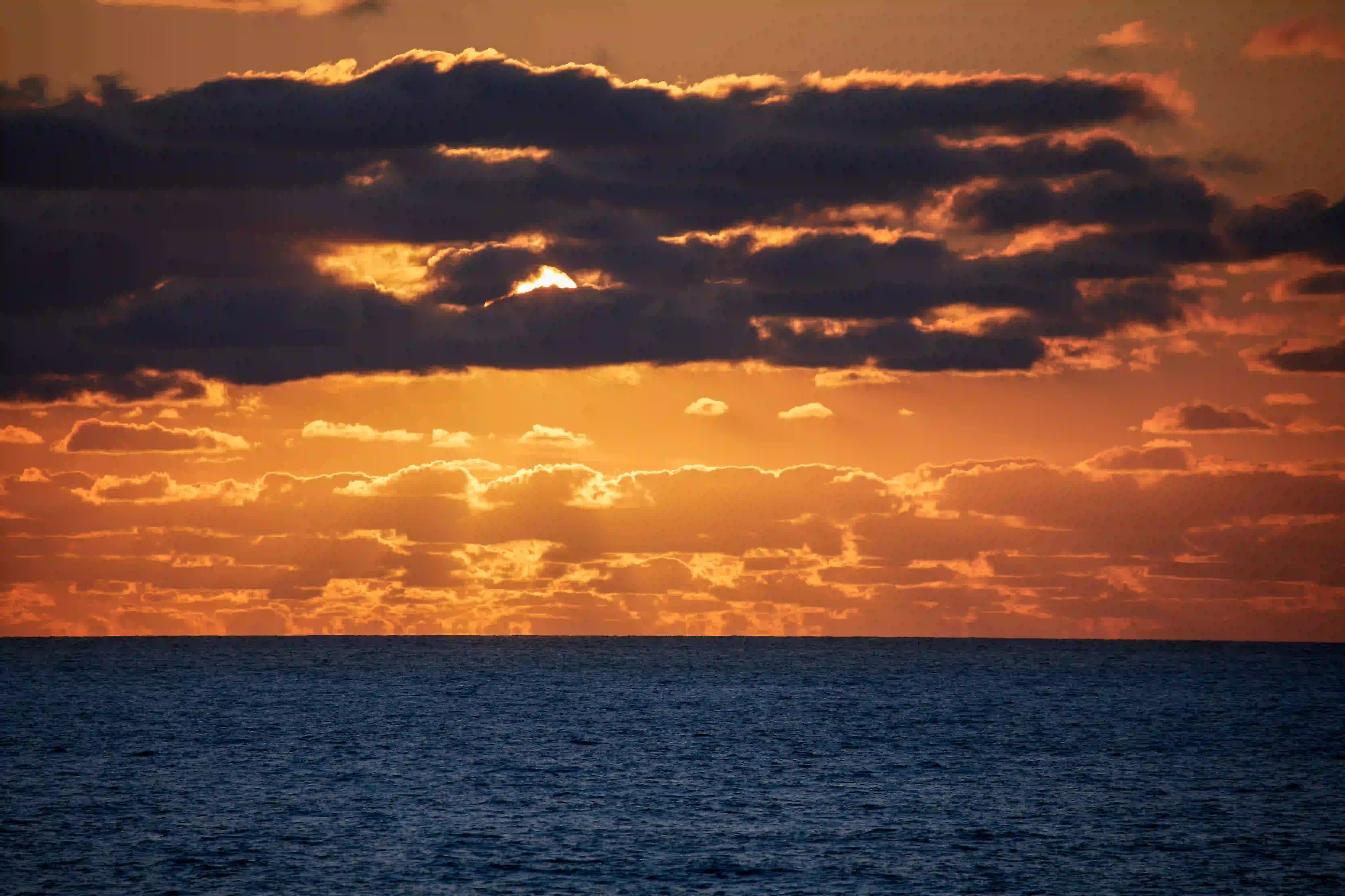 Orange sunset with dark clouds over a calm ocean horizon.
