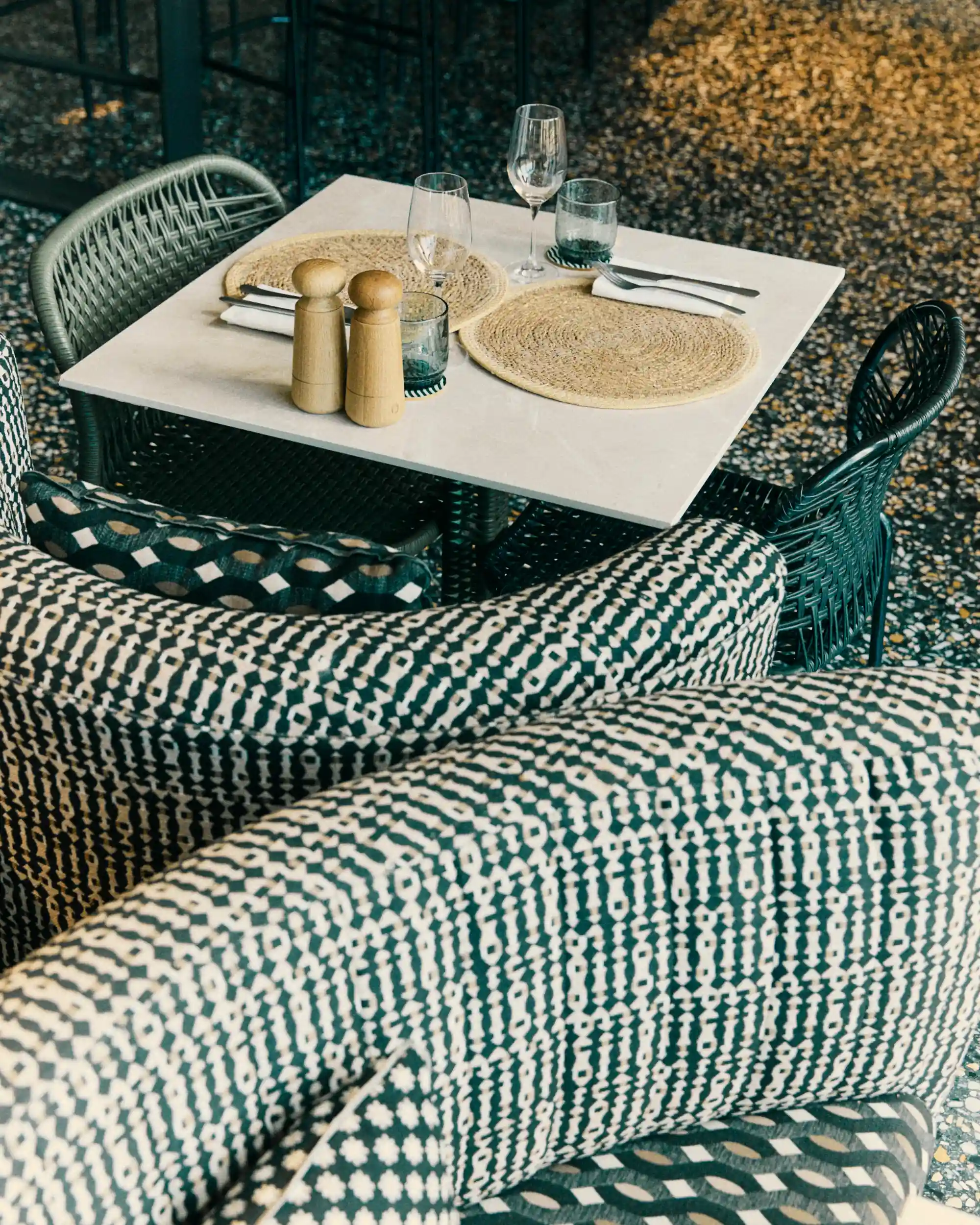 Cozy restaurant interior with curved banquette, wicker chairs, set tables, and a woven pendant light.