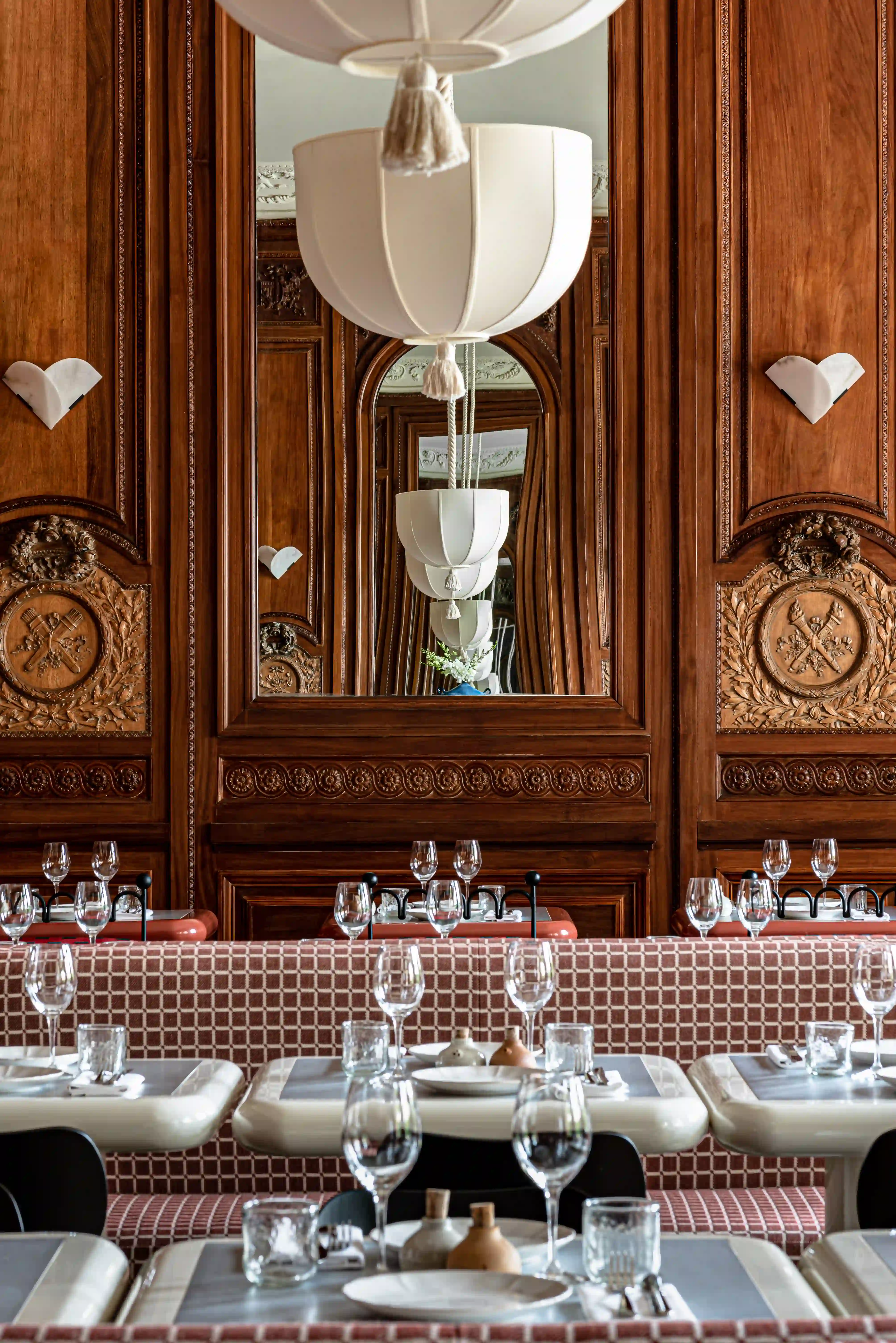 Restaurant table set with plates and glasses beside ornate wood paneling and red cushioned chairs.