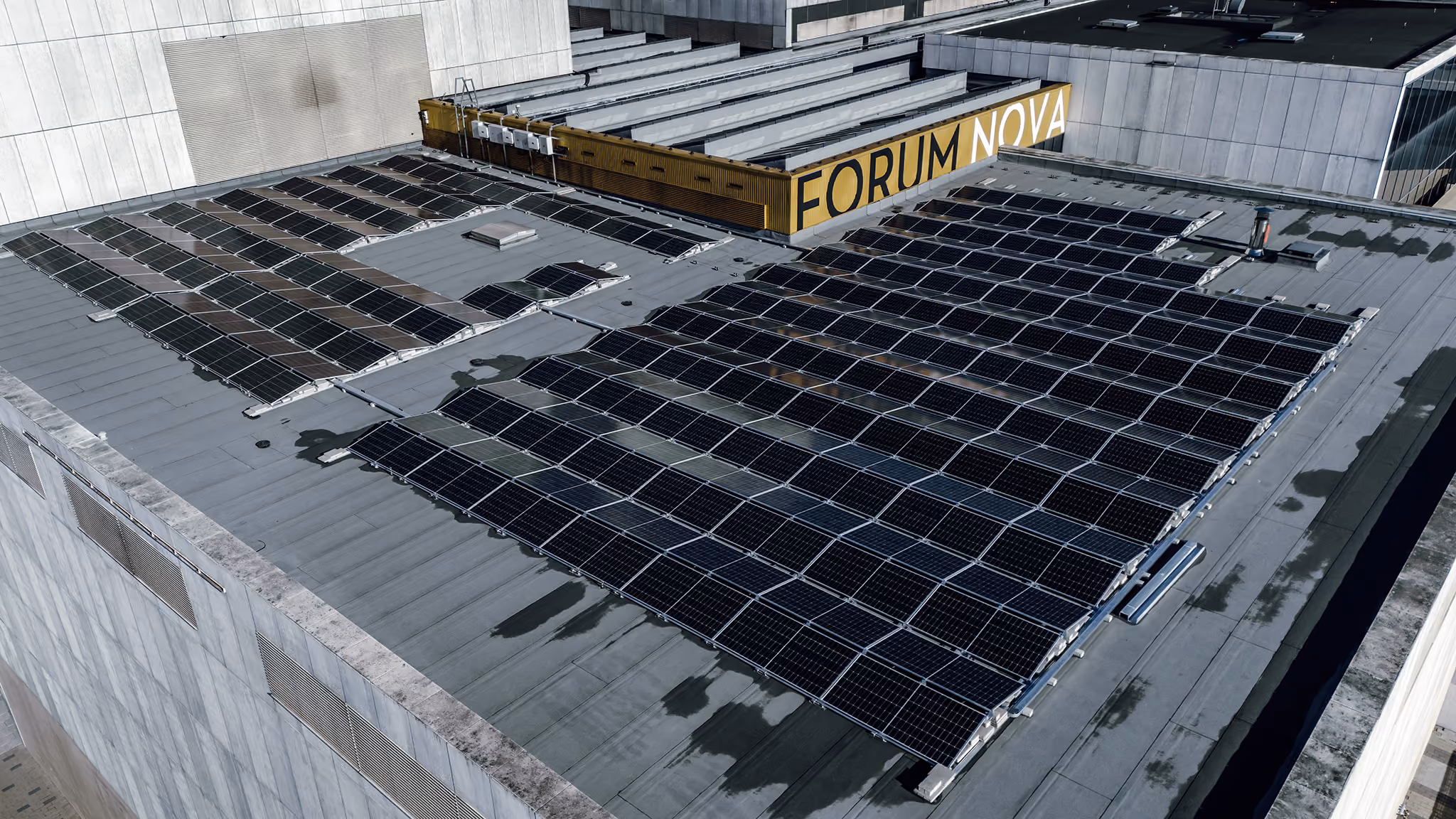Rooftop solar panels installed on a flat building roof with a yellow sign reading 'FORUM NOVA' in the background.