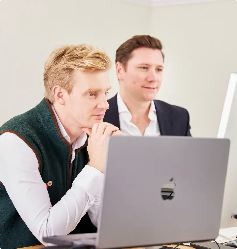 Two men focused on work, looking at a laptop screen in a bright office setting.