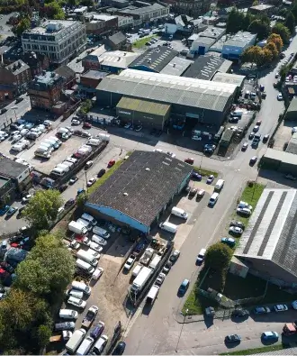 Aerial view of an industrial complex with multiple warehouses, parking lots filled with cars and trucks, and surrounding roads.