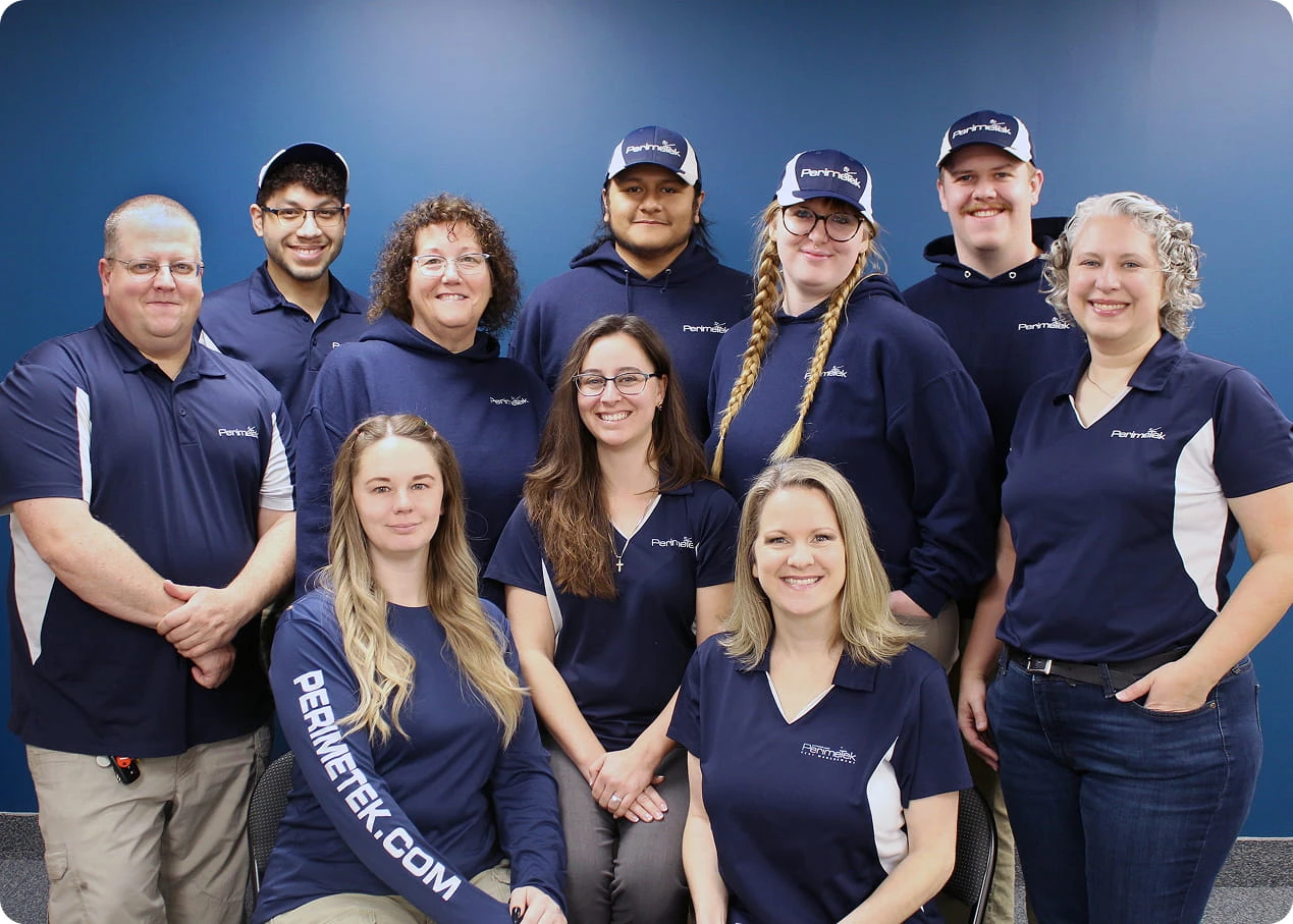 Group of eight PerimeTek employees in navy uniforms posing in front of a blue wall with the company logo and holding a sign that reads 'CNY Business Journal Best Places to Work 2024'.