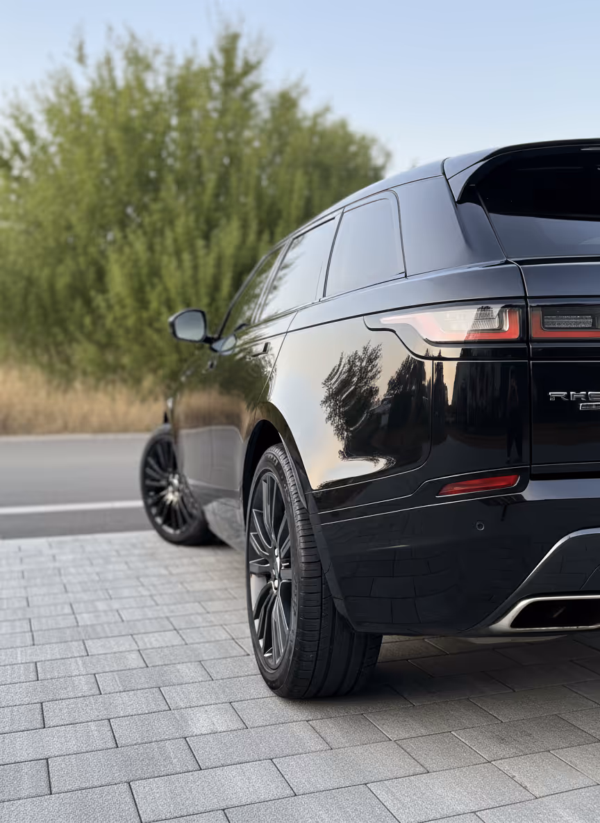 Vue arrière latérale d'un SUV noir garé sur un trottoir en pavés avec arbres en arrière-plan.
