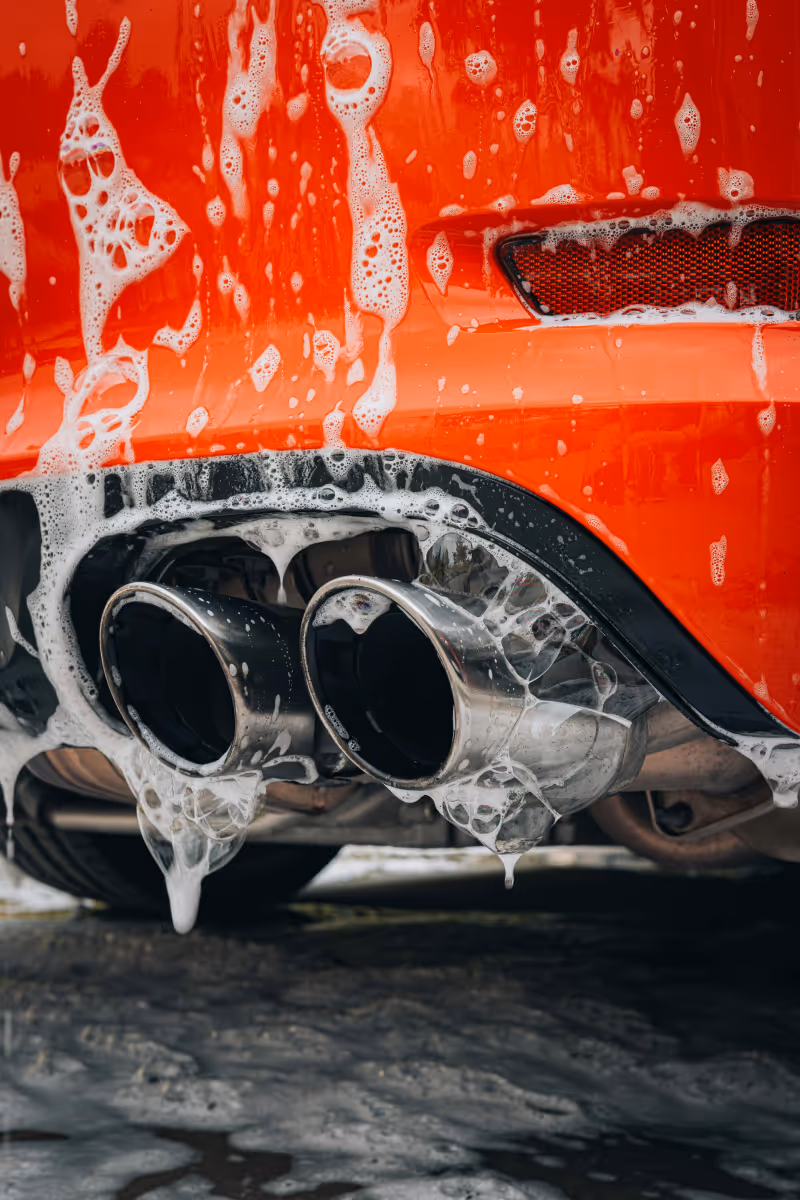 Gros plan sur les doubles sorties d'échappement en métal chromé d'une voiture rouge recouvertes de mousse de lavage.