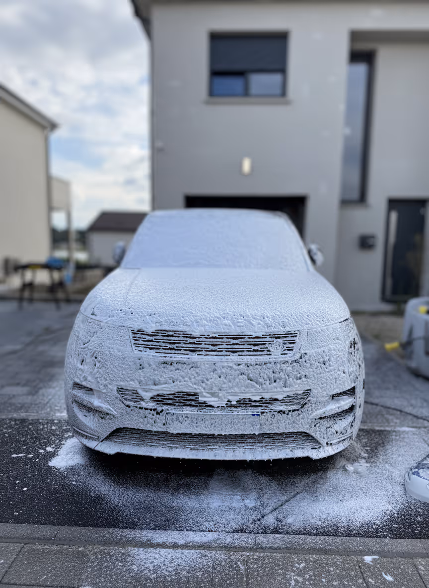 Voiture couverte de mousse blanche de lavage sur une allée devant une maison moderne.