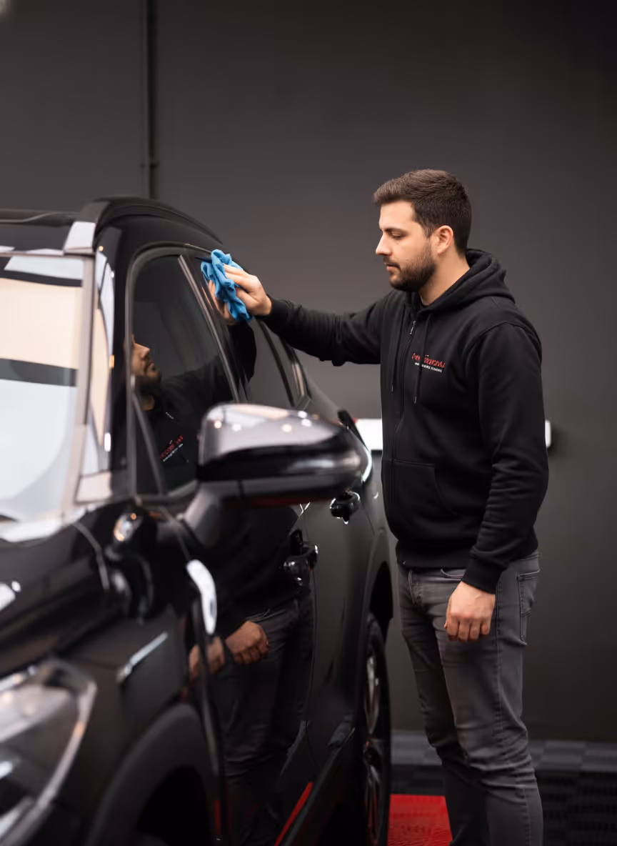 Homme nettoyant une voiture noire avec un chiffon bleu dans un atelier sombre.