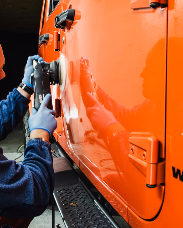 Personne utilisant une polisseuse électrique pour polir la porte orange d'un véhicule.