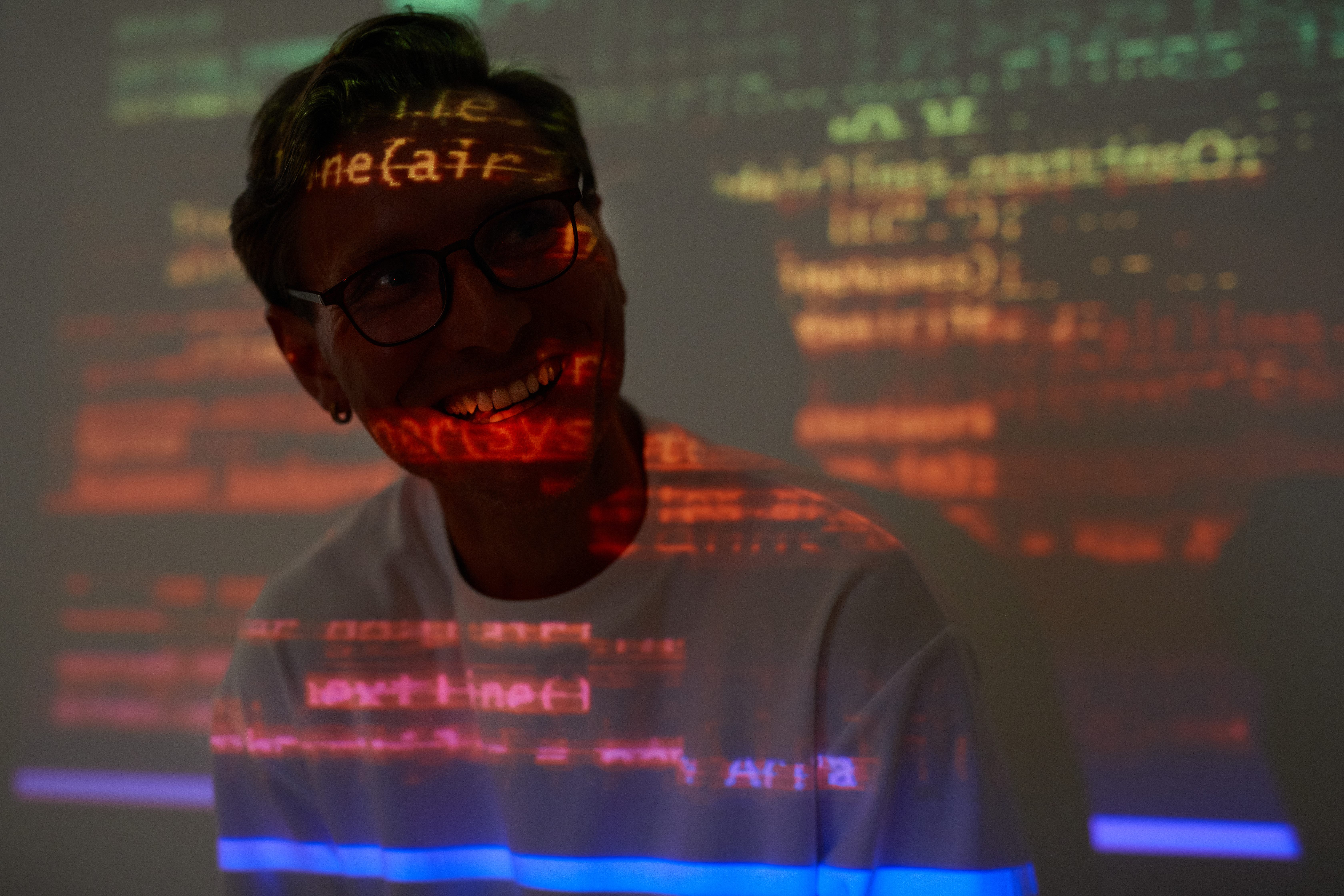 Persona sorridente davanti a codice informatico proiettato: immagine su programmazione, sviluppo software, intelligenza artificiale e innovazione digitale.