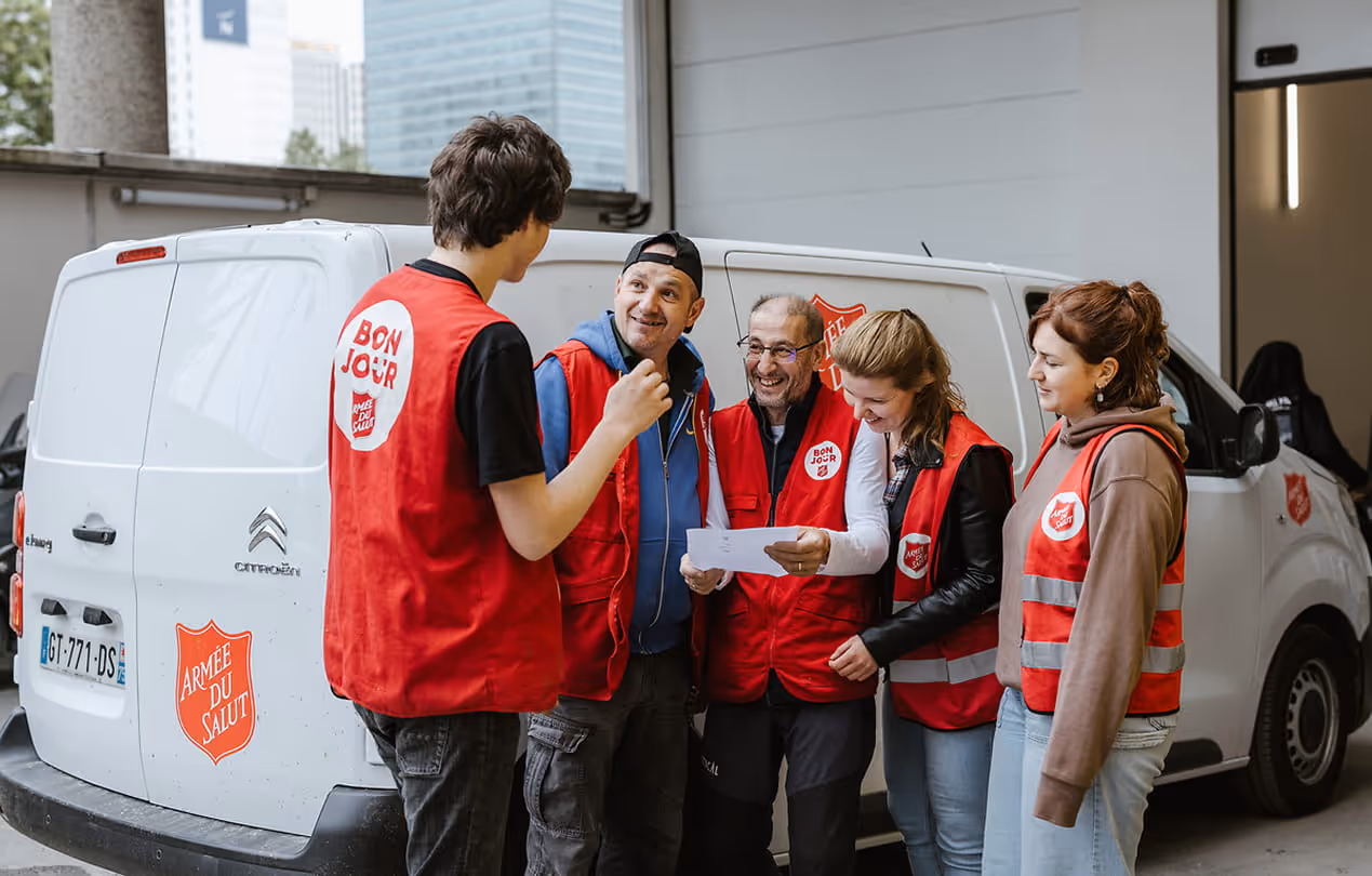 énévoles de l'Armée du Salut en gilets rouges échangeant devant un véhicule de secours alimentaire.