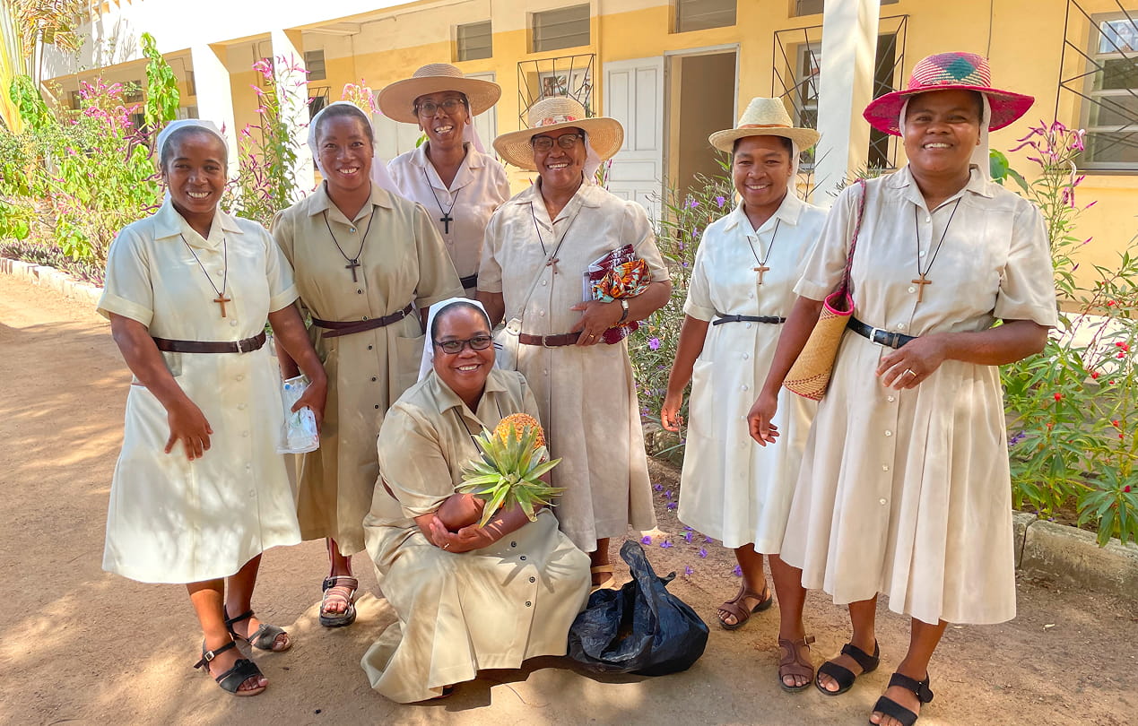 Groupe de sept femmes encadrantes souriantes, en tenue claire avec des chapeaux, posant devant les bâtiments de l'orphelinat à Madagascar.