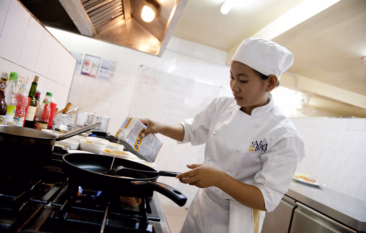 Élève de l'école Sala Baï cuisinant avec un wok dans une cuisine professionnelle de formation hôtelière.