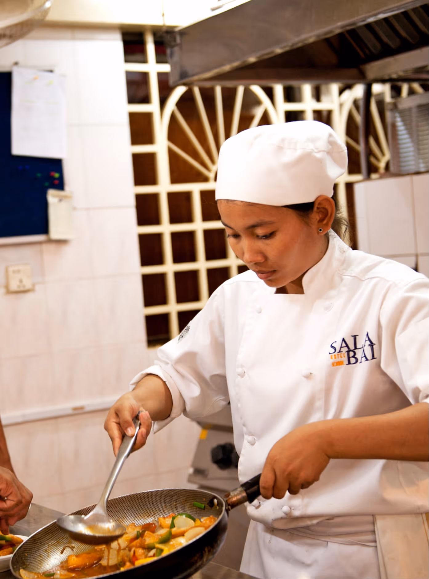 Chef cuisinière préparant un plat sauté dans une école de restauration, illustrant la formation aux métiers de bouche.