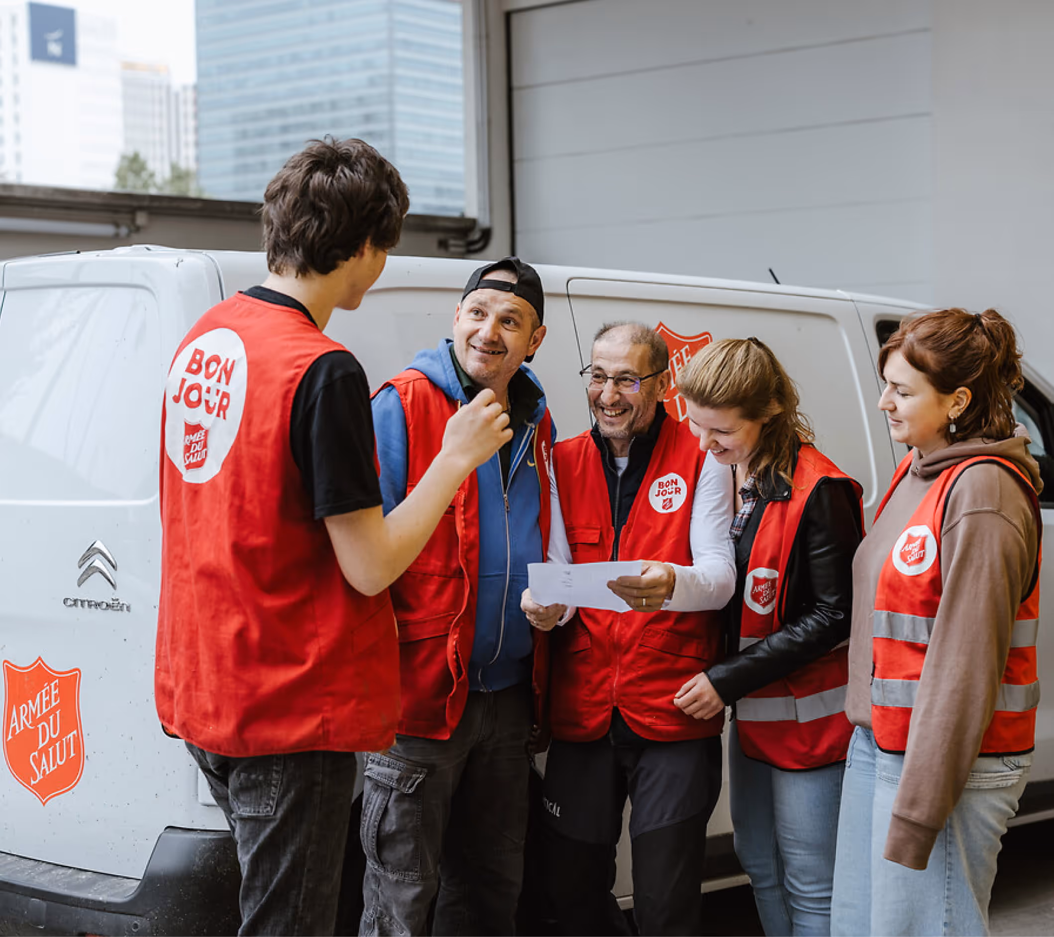 Bénévoles de l'Armée du Salut en gilets rouges discutant devant un véhicule de distribution alimentaire.