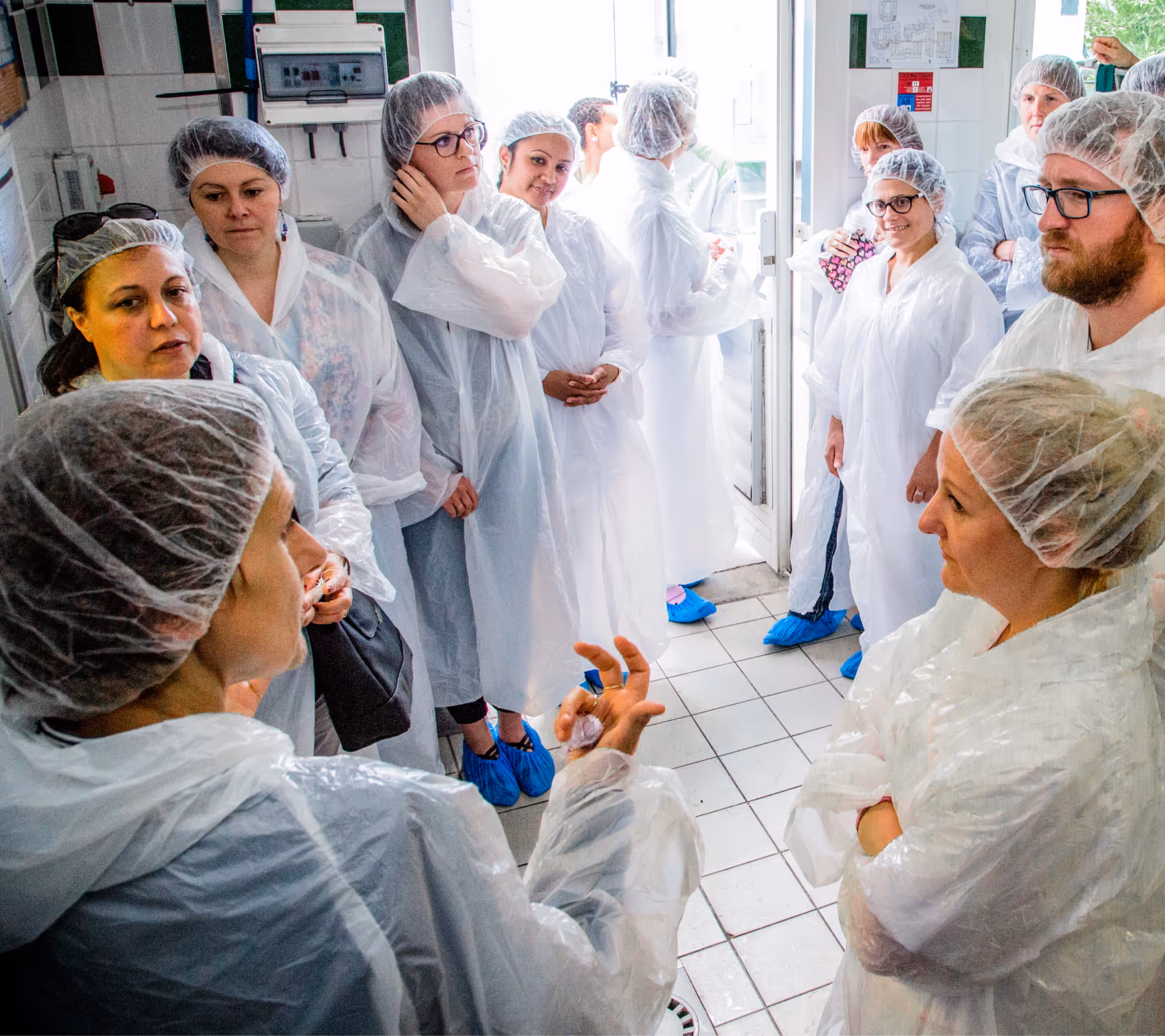Groupe de professionnels en tenue d'hygiène blanche échangeant dans une cuisine, illustrant le partage d'expertises.