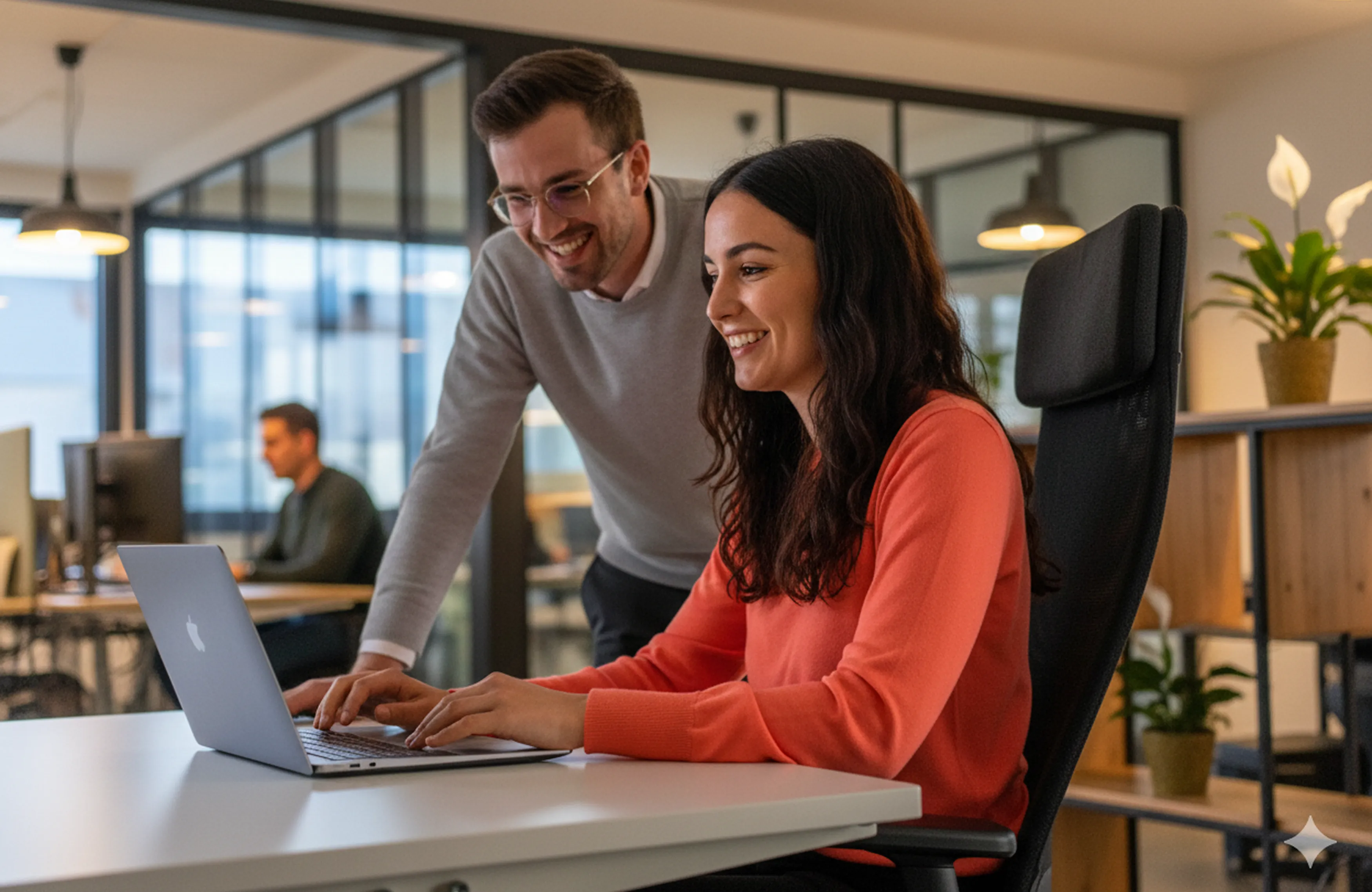 Deux collaborateurs du groupe Positive souriants travaillant ensemble sur un ordinateur portable dans un bureau moderne.
