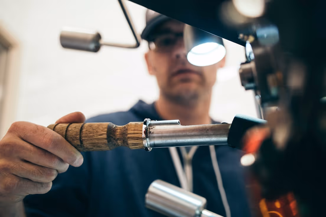Person operating a machine with a wooden handle under a bright work light.