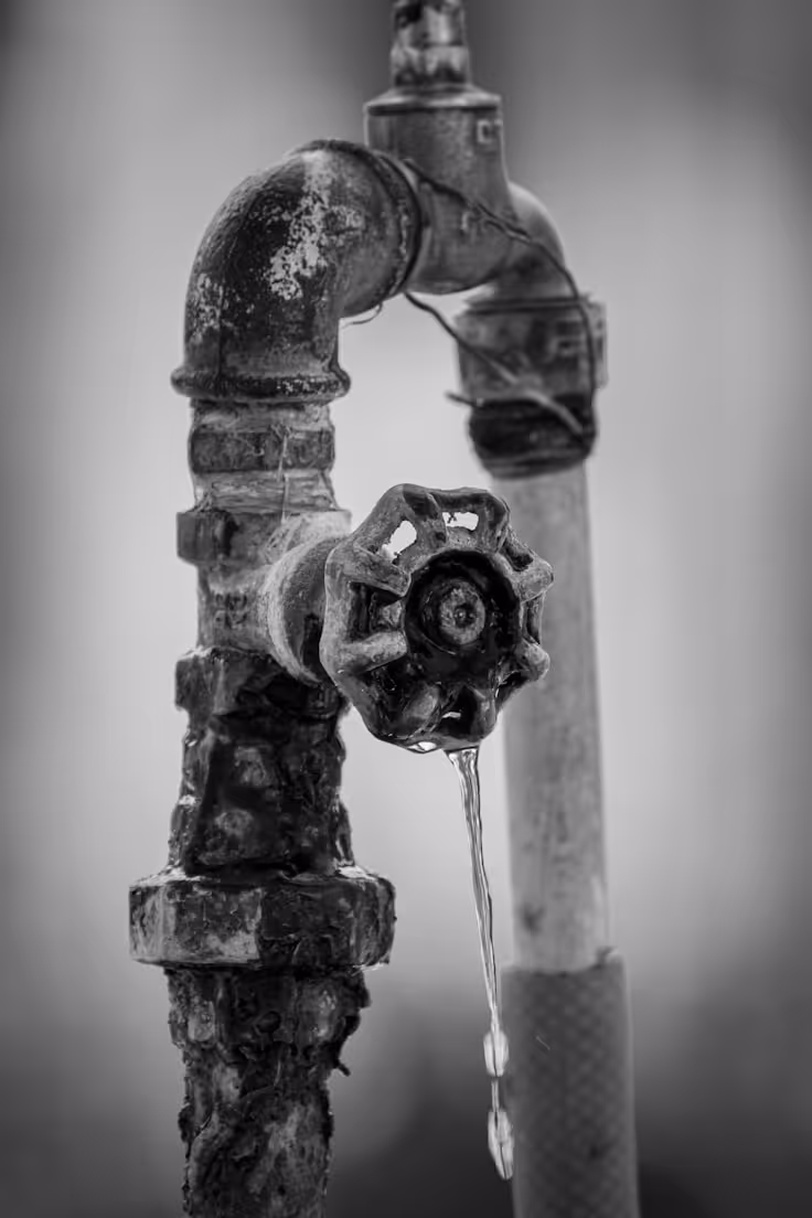 Close-up of an old, rusty metal water faucet with a small stream of water dripping from the valve.