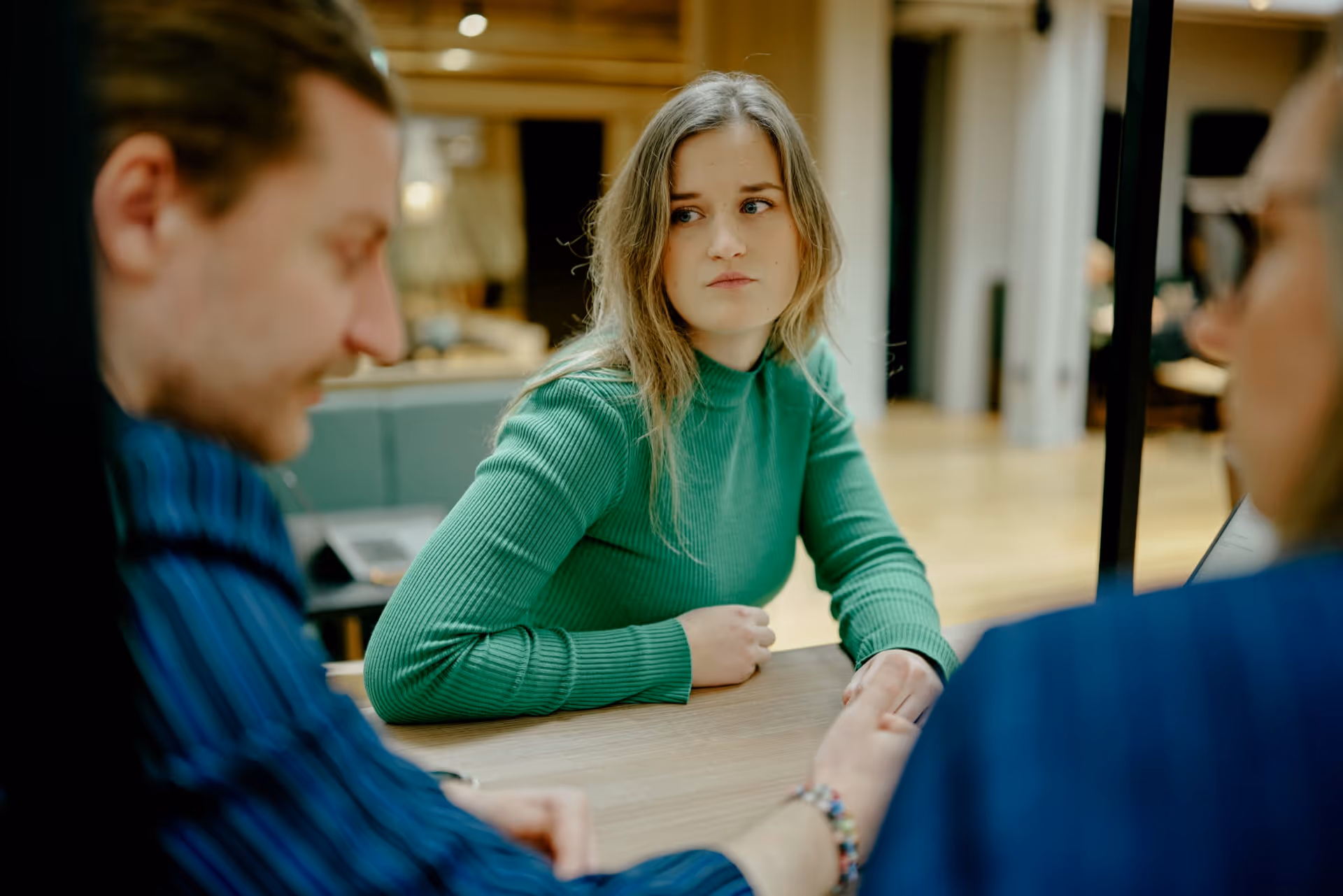 Young woman in green sweater sitting at a table looking thoughtfully at a man holding her hand.