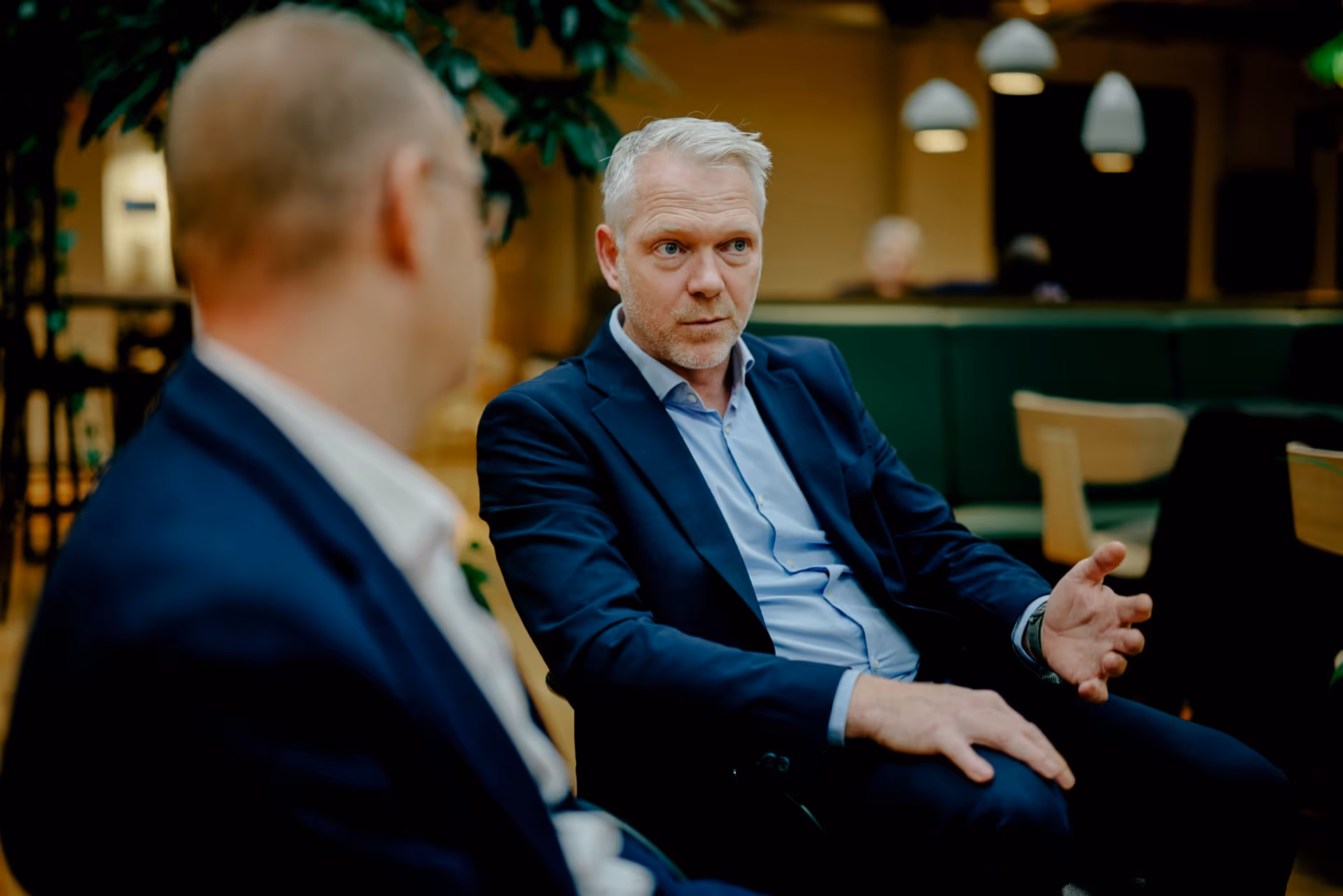Two businessmen in suits engaged in a serious conversation in a modern office lounge.