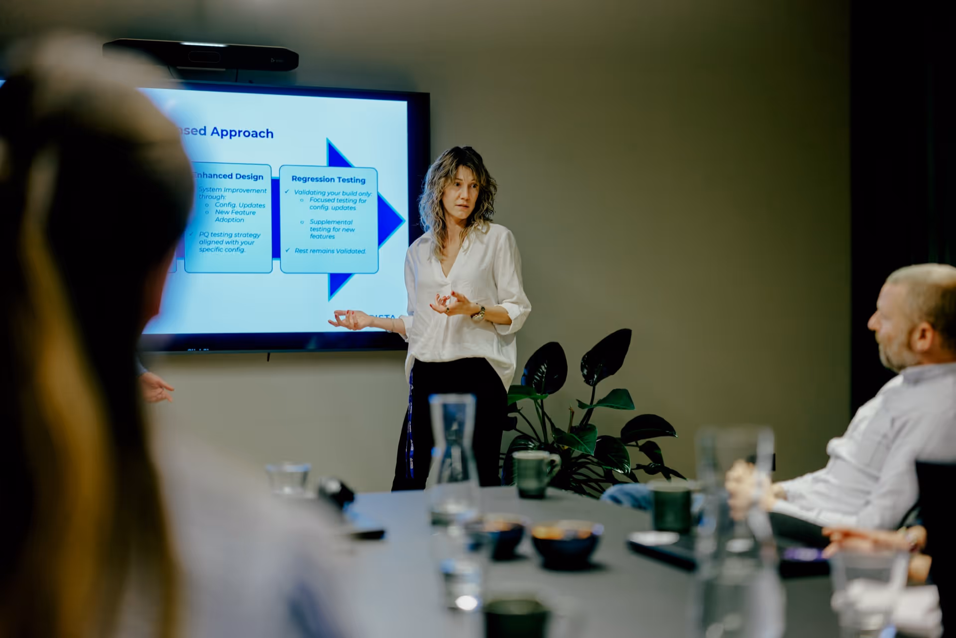Woman in white blouse presenting a flowchart on a screen to a seated group in a meeting room.