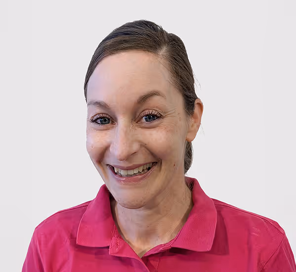 Frau mit zusammengebundenen braunen Haaren und rosa Polohemd lächelt frontal in die Kamera vor hellem Hintergrund.