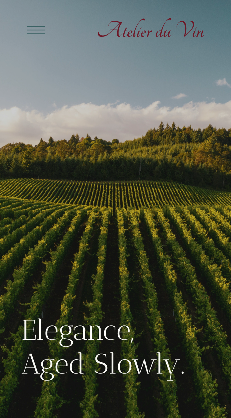 Vineyard rows under a blue sky with text 'Elegance, Aged Slowly' and the name Atelier du Vin.