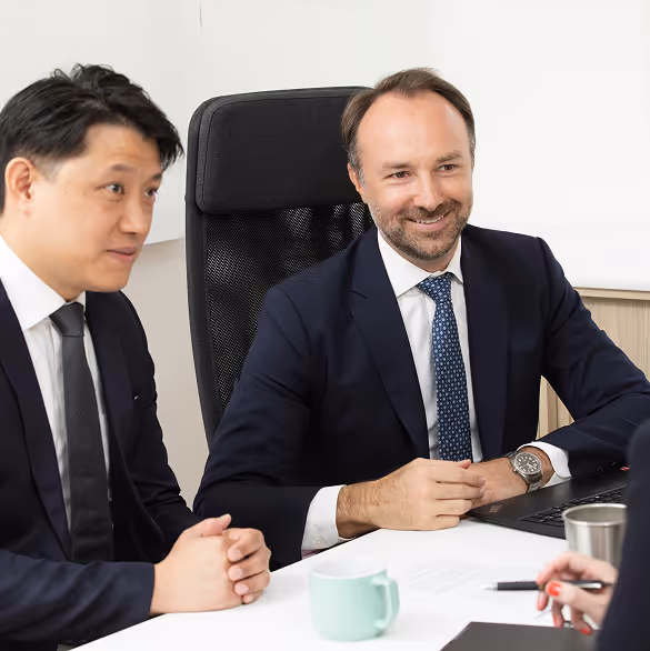 Two men in business suits sitting at a table engaged in a meeting with a third person.