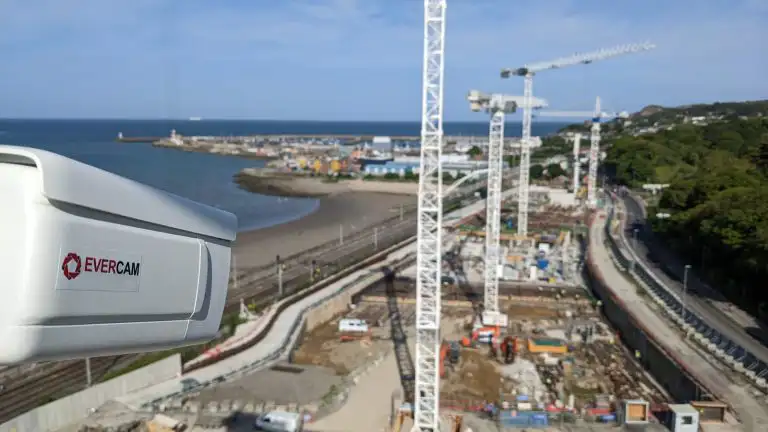 Evercam construction camera installed on a pole overlooking an active coastal construction site with cranes, roadworks, and heavy equipment.