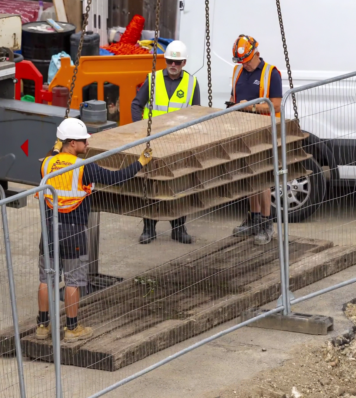 Construction workers wearing protective equipment lifting and positioning building materials within a secured site.