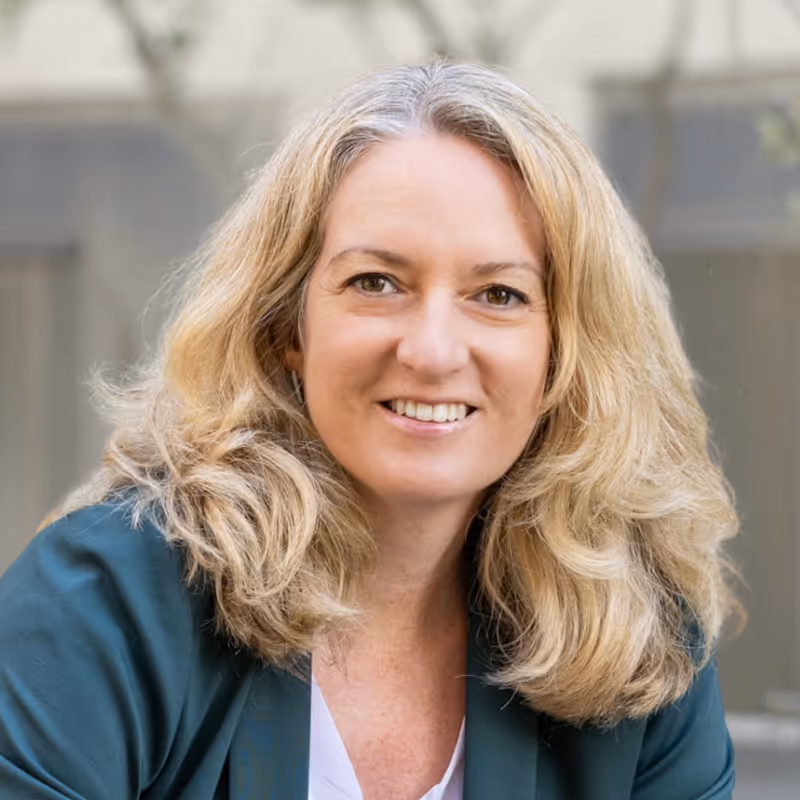 Coach Claudia Alban – Smiling woman with shoulder-length blonde hair wearing a dark green blazer and white shirt.