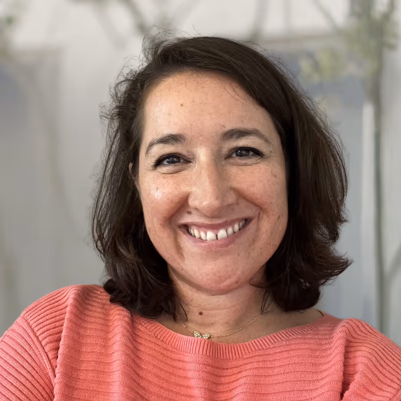 Coach Anne-Sophie Murset – Smiling woman with shoulder-length dark hair wearing a coral ribbed sweater and gold necklace.