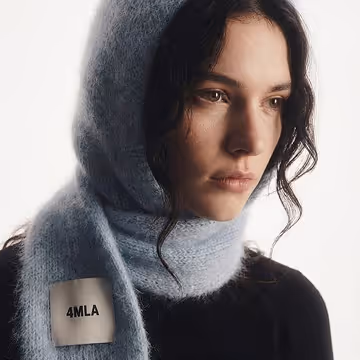Woman with dark hair wearing a soft blue scarf wrapped around her head and neck against a white background.