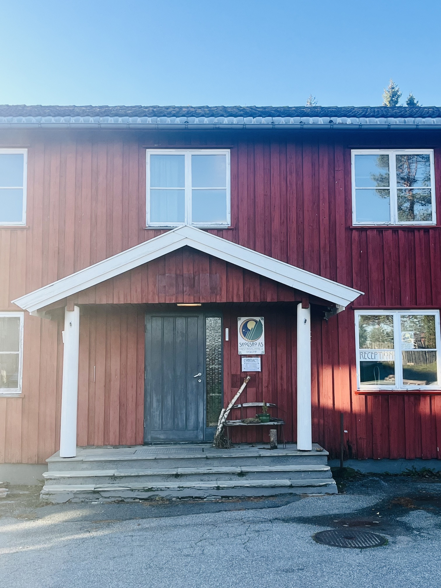 Rødt to-etasjes bygg med grå inngangsdør, hvite søyler og skilt for Skogsro AS og resepsjon.