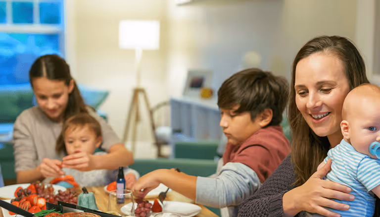 A family of two women and three children enjoying a meal together in a cozy living room.