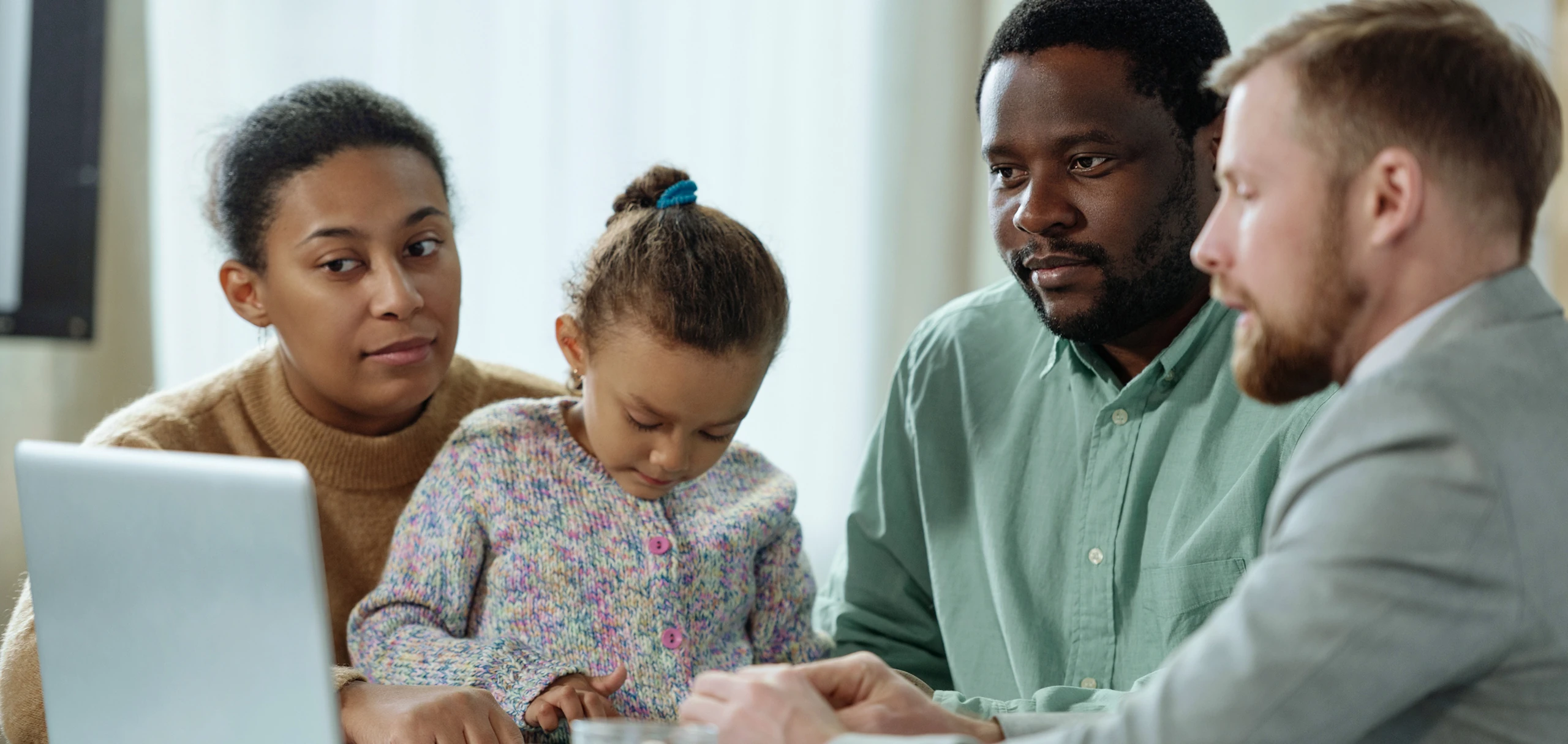 Young girl using a tablet while two adults and a man in a suit sit nearby, engaged in discussion.