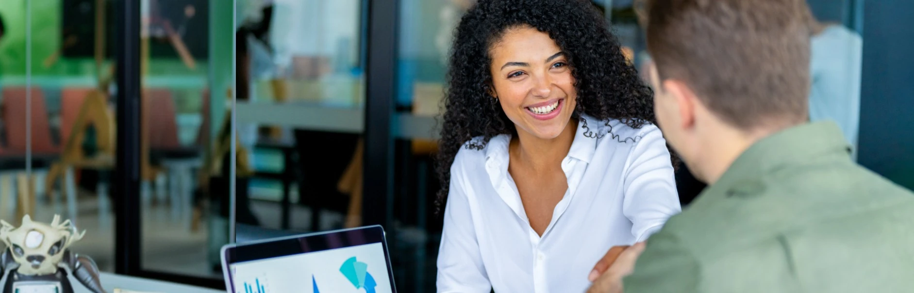 Smiling woman showing a presentation on a laptop to a man in a modern office setting.