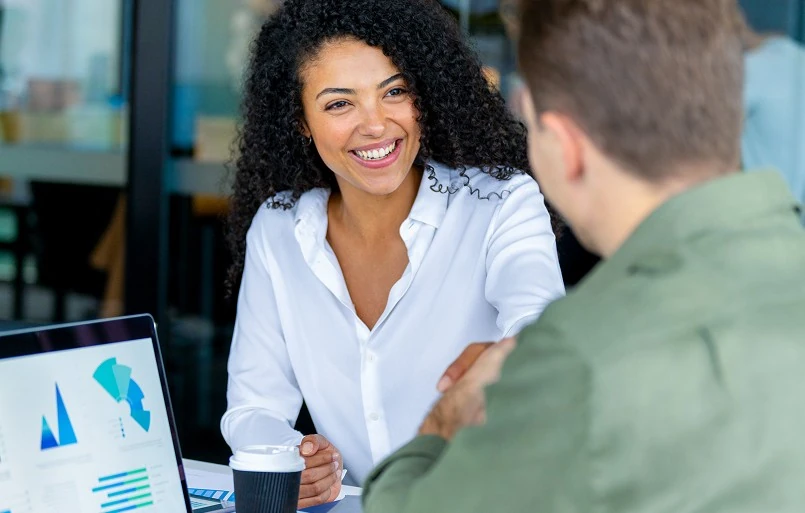 Smiling woman showing a presentation on a laptop to a man in a modern office setting.