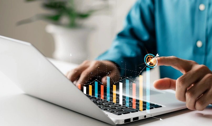 Person using a laptop with a digital bar chart and target graphic overlay on the keyboard.